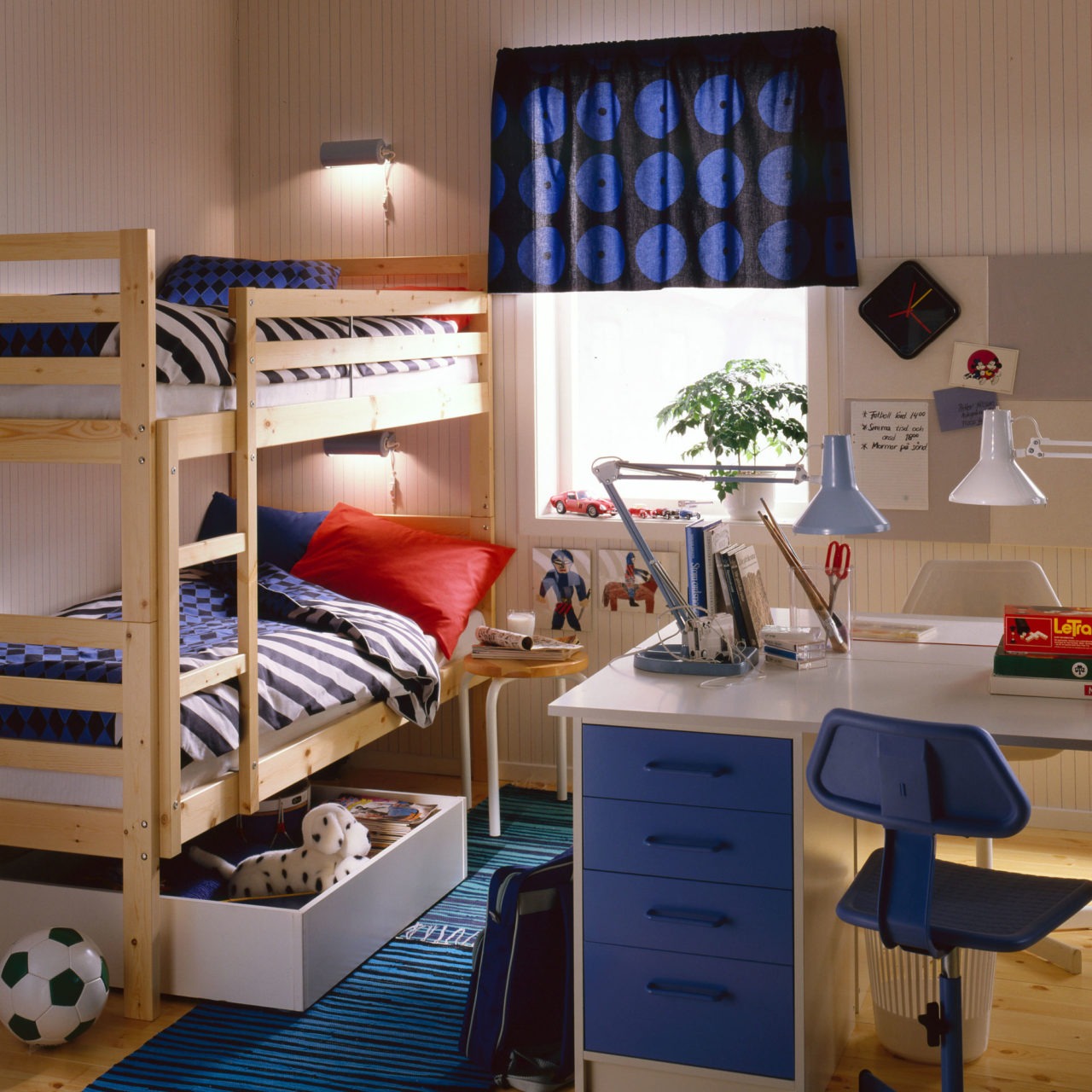 Ett ljust barnrum med våningssäng, modell REKDAL, och golv i ljust trä. Spridda leksaker och ett vitt skrivbord, modell BOJ.