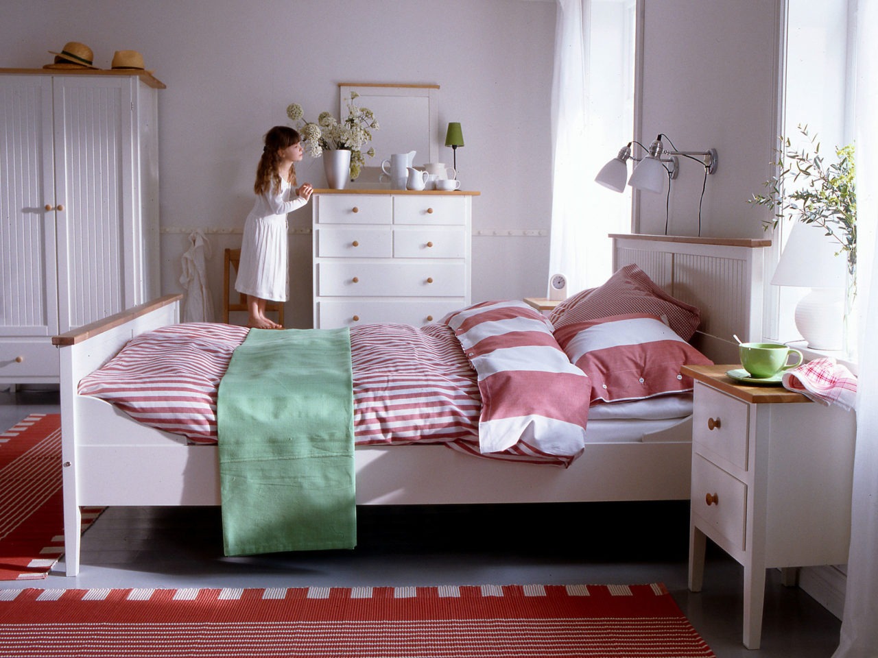 En flicka står på en stol och kikar ut från ett sovrum med möbler helt i vitt, modell VISDALEN, i modern allmogestil.