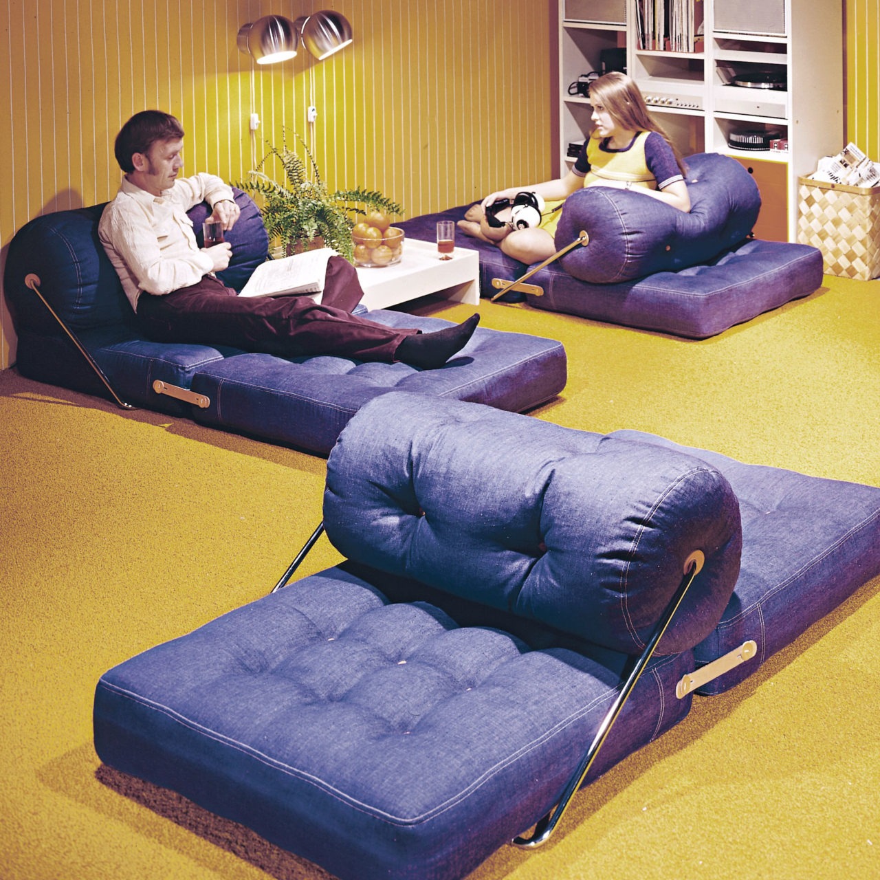 Jeanstygklädda plymåer, modell TAJT, utvikta som divaner och utspridda på golvet i ett rum med gul heltäckningsmatta.