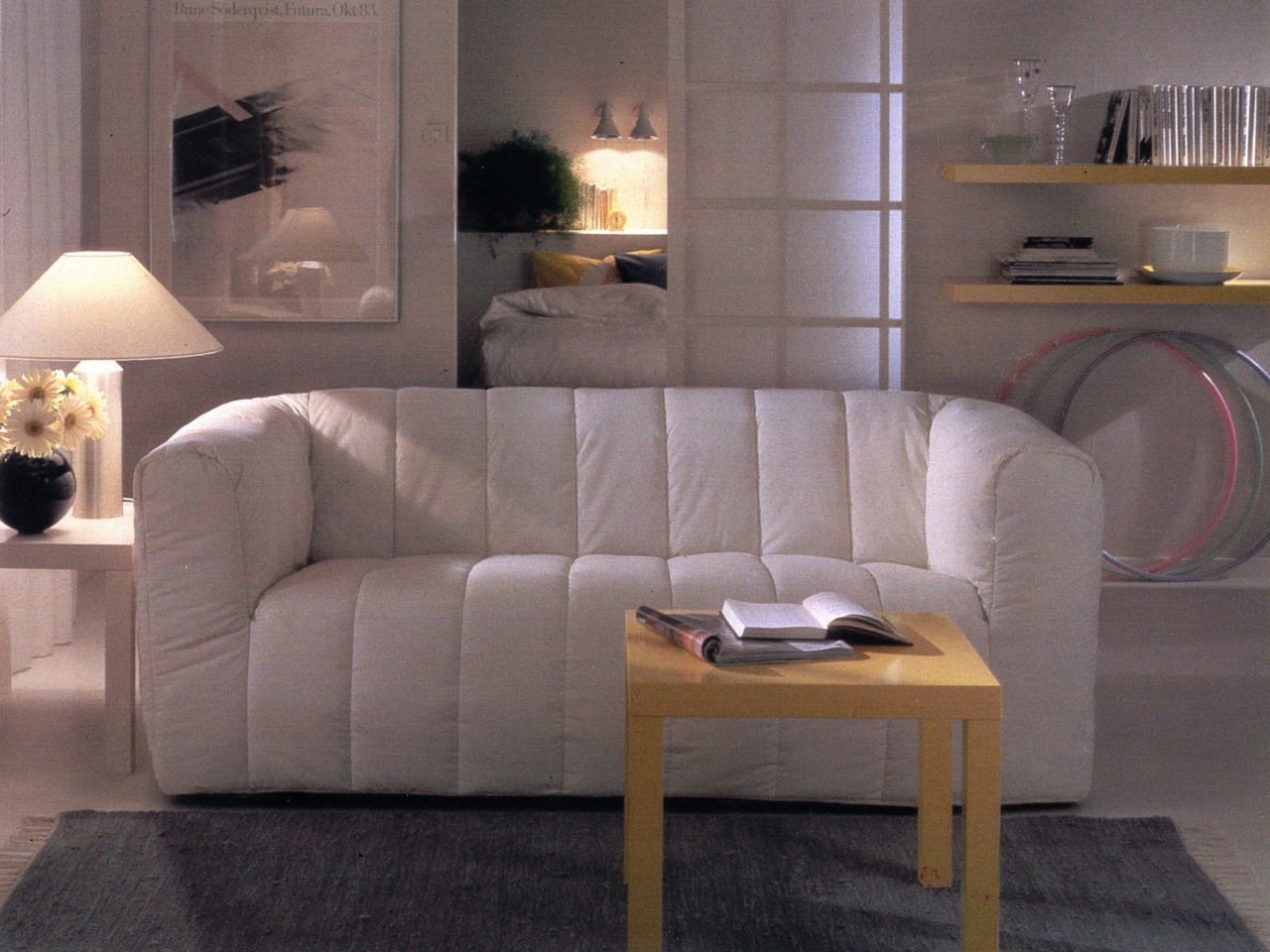 Weißer Raum mit massigem, weißem KLIPPAN Sofa in der Mitte. Couchtisch und Wandregale aus hellem Holz, Modell LACK.