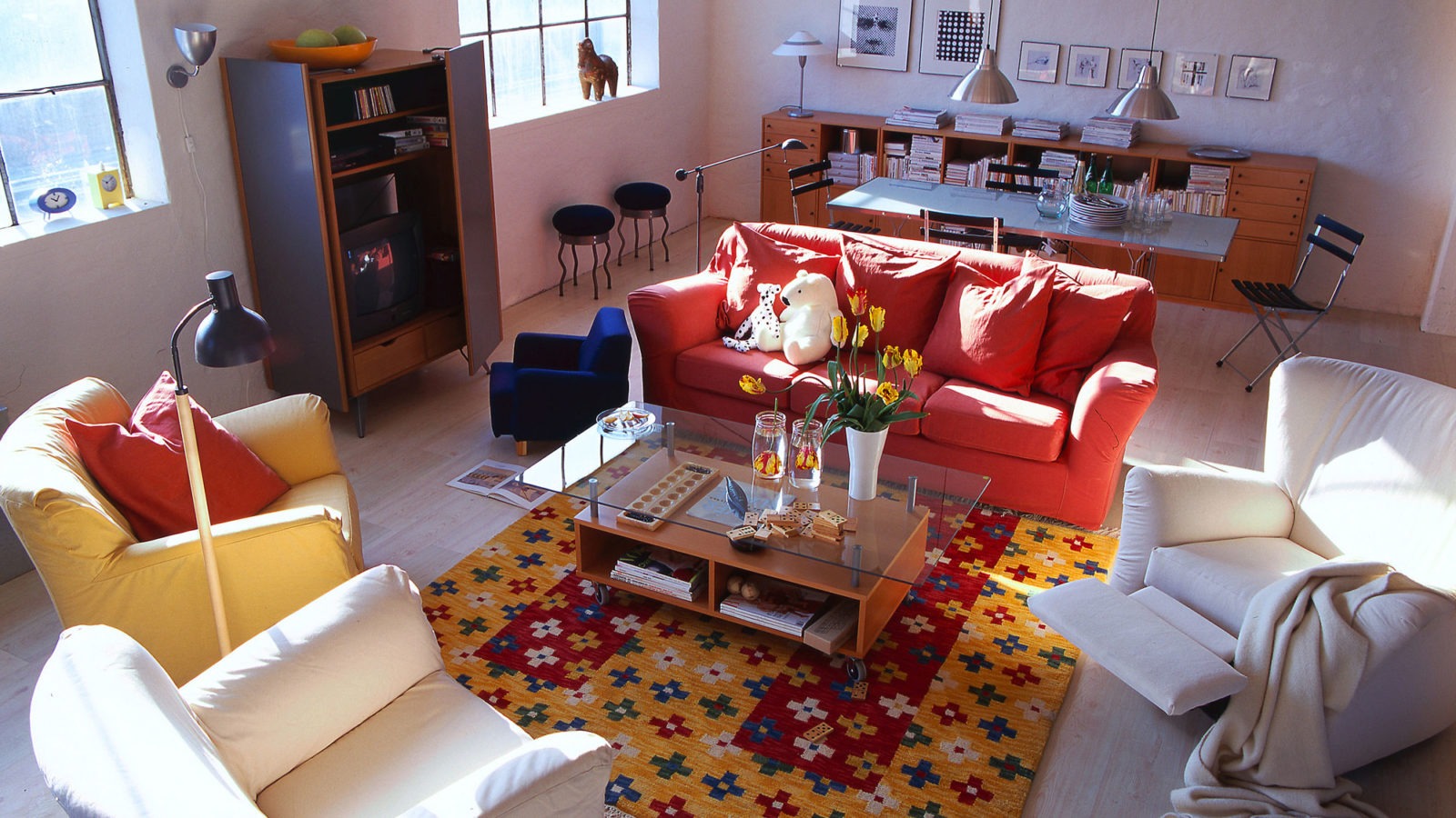 Ett stort vardagsrum med en olikfärgad sittgrupp av soffor och fåtöljer runt ett soffbord med förvaring och glasskiva.