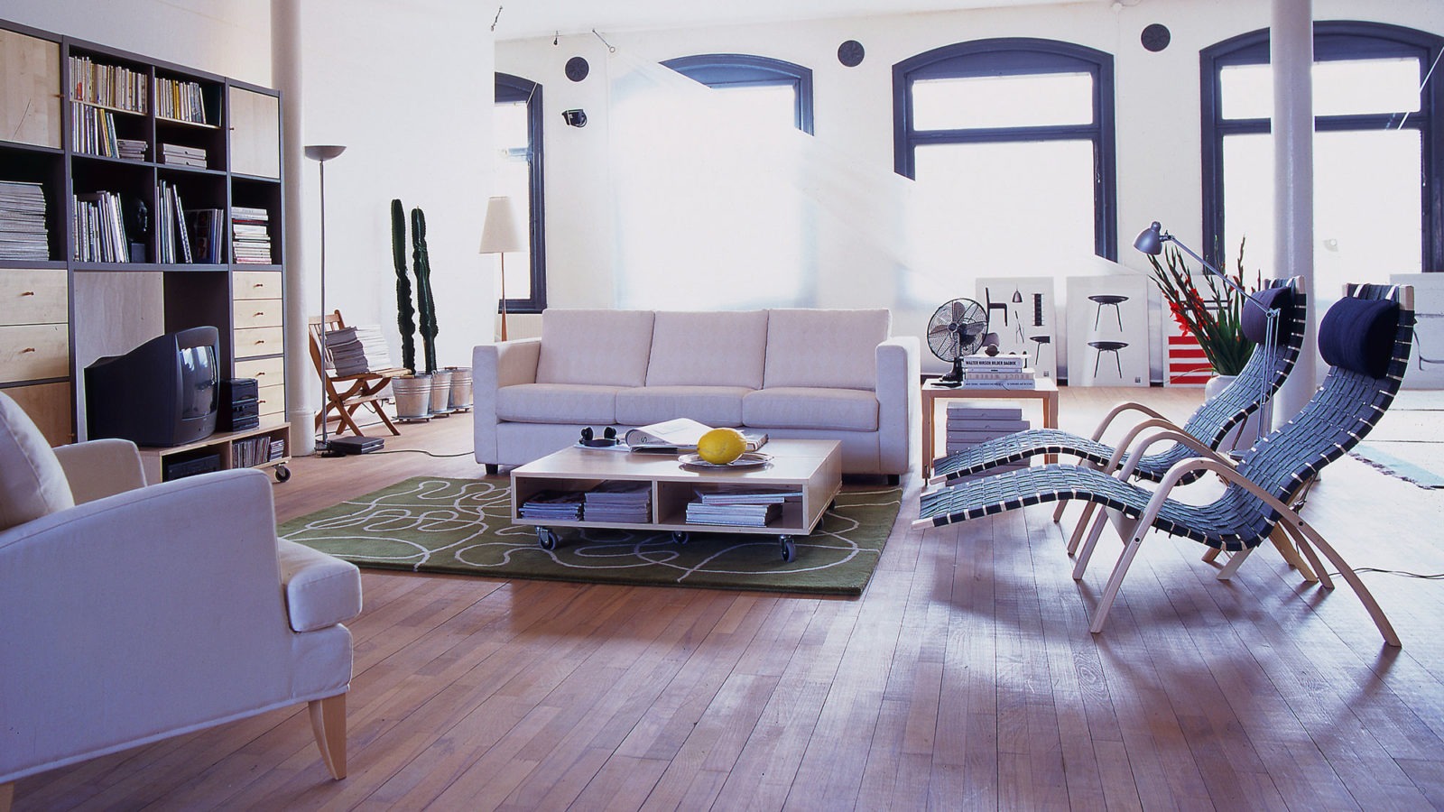 Grande pièce avec piliers et parquet. Table basse sur roulettes, un canapé, un fauteuil et deux chaises longues.