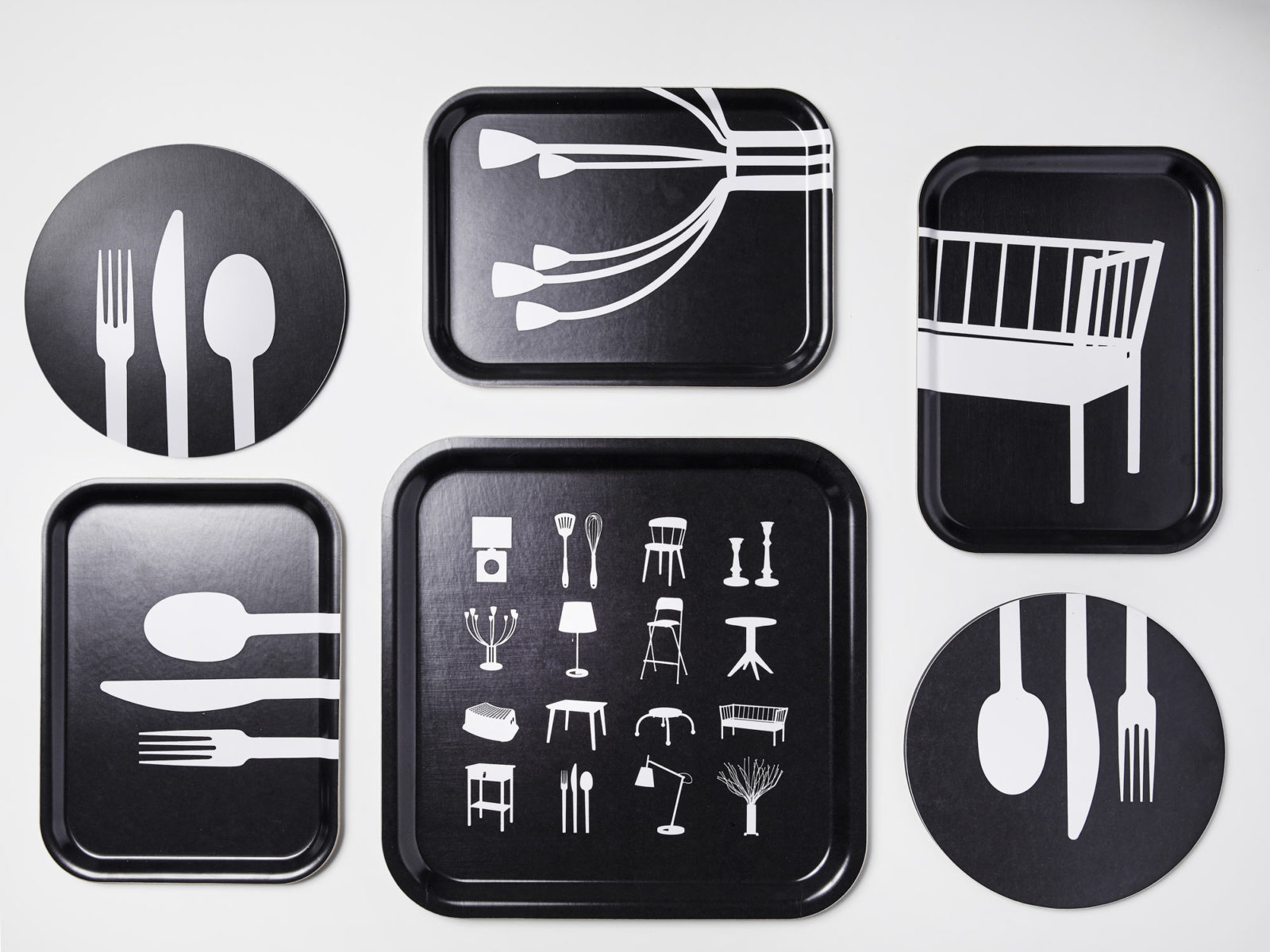 Trays and pot holders with black and white stylised pattern with silhouettes of home furnishing products.