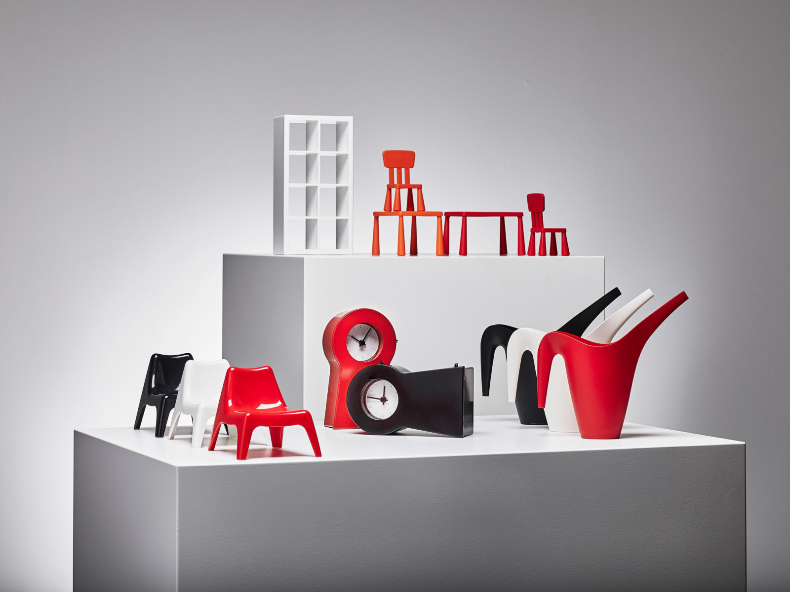 Miniatyrer av möbler och dekorativa föremål i rött och svart, inklusive en klocka, uppställt på två vita kuber.