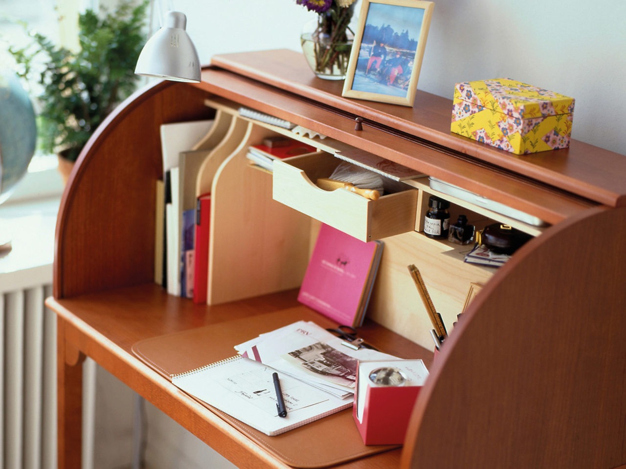 Brown bureau filled with papers, books, photos and decorative items.