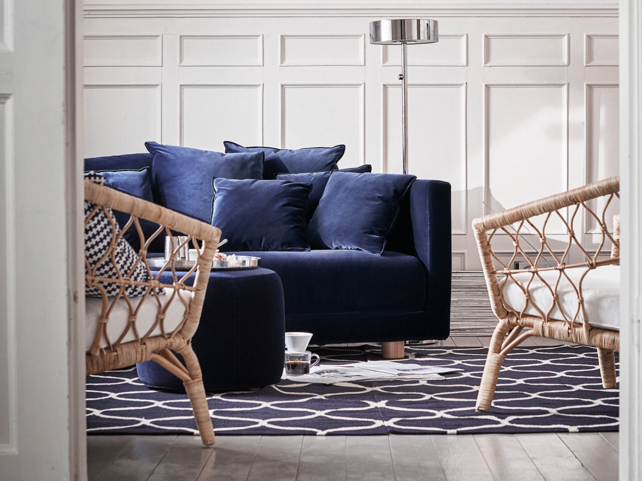 Two rattan armchairs stand opposite the blue velvet sofa, a blue pouffe is used as a coffee table.