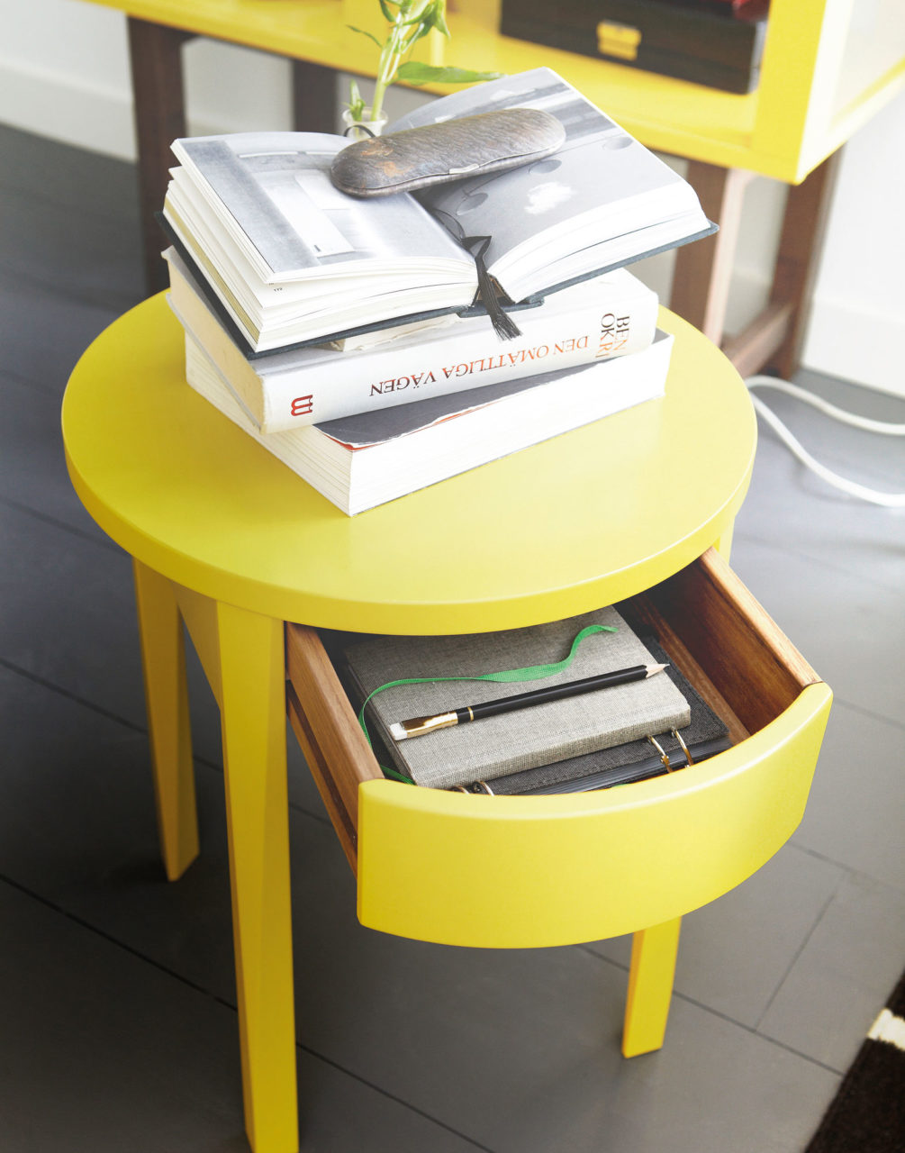 Round yellow side table with drawer, a stack of books on top.