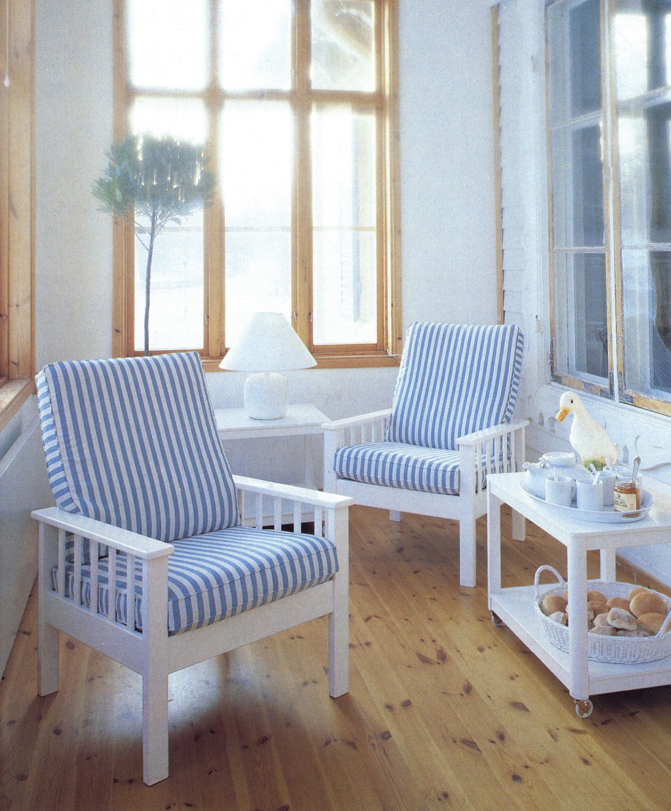 Light room with big windows, hardwood floors, two armchairs with blue and white striped cushions.