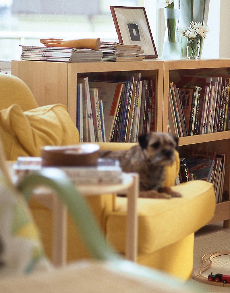 Detaljbild från rum som visar bekväm gul fåtölj och låg bokhylla.