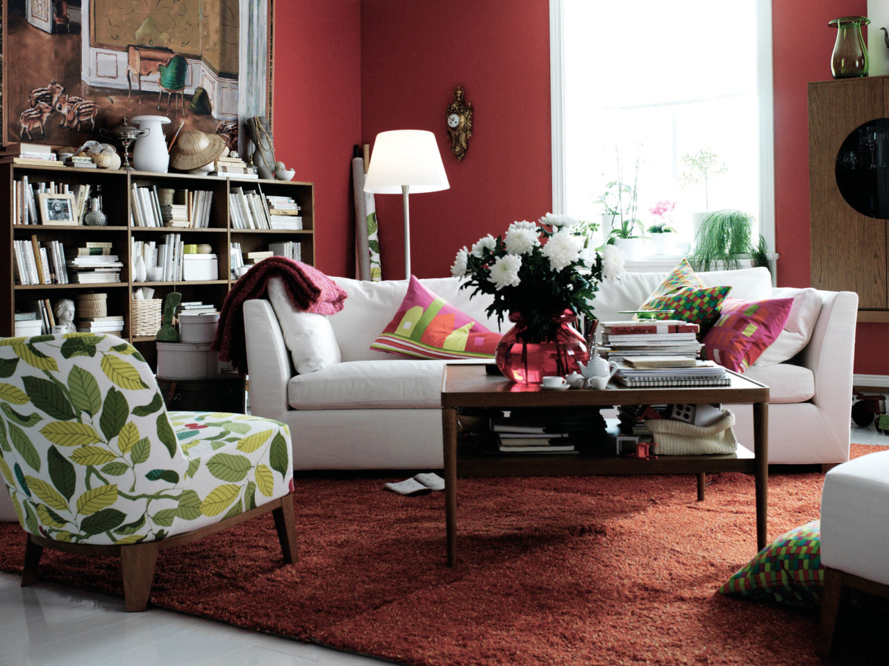 Vardagsrum med sittgrupp, bokhylla, orange matta och vinröda väggar.