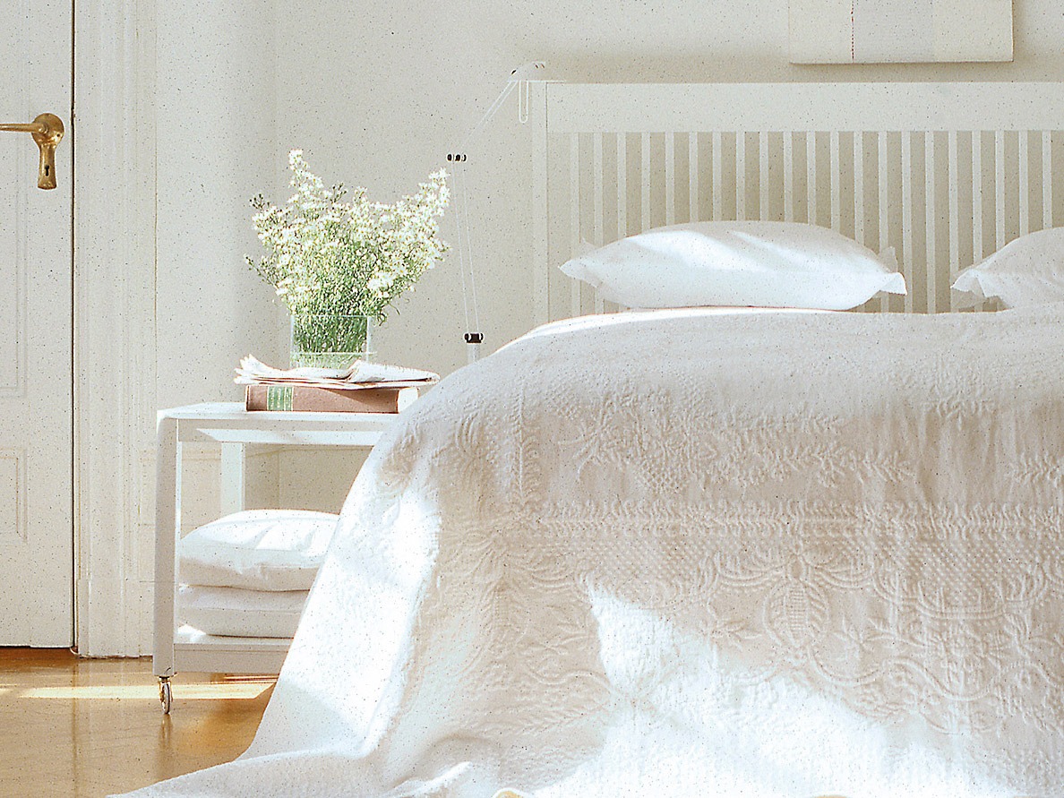 Luftigt och ljust sovrum med överkast, gardiner och kuddar i vitt.