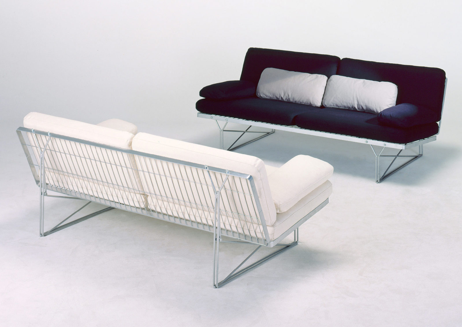Two simple sofas, one white, one black, with a steel mesh underframe.