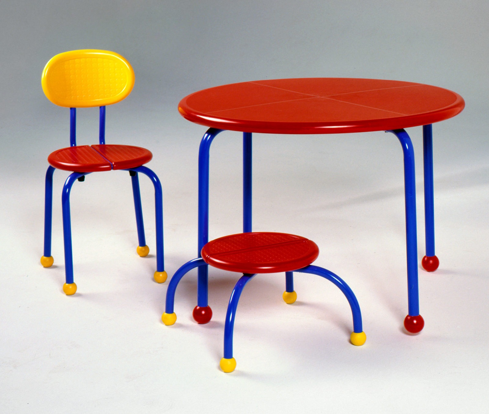 Barnmöbler i klara färger, rött, gult och blått - ett bord, en stol och en låg pall.