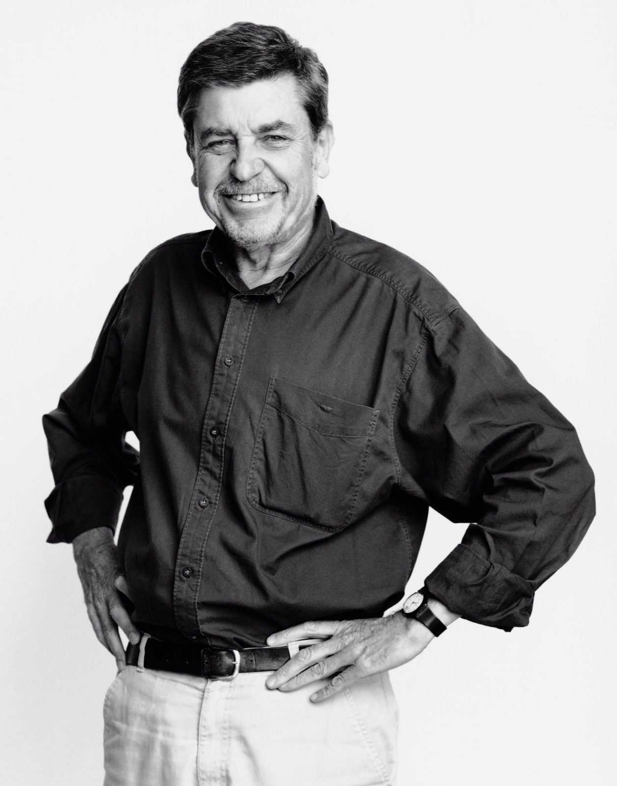 A smiling, dark-haired Tomas Jelinek, dressed in a dark shirt and light trousers, stands with hands on hips.