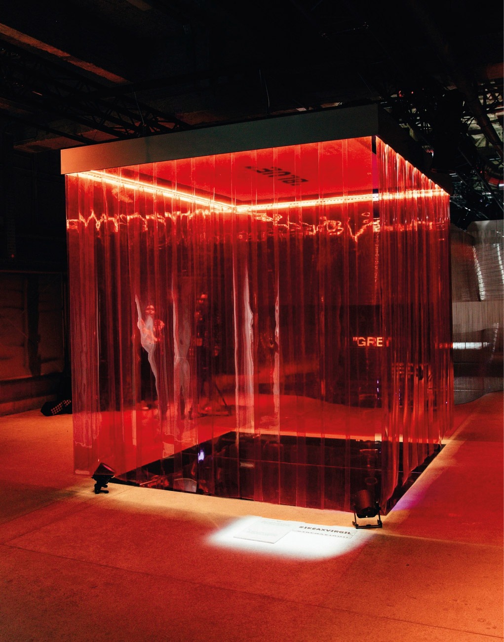Art installation of plastic cube illuminated by red and white light in dark room.