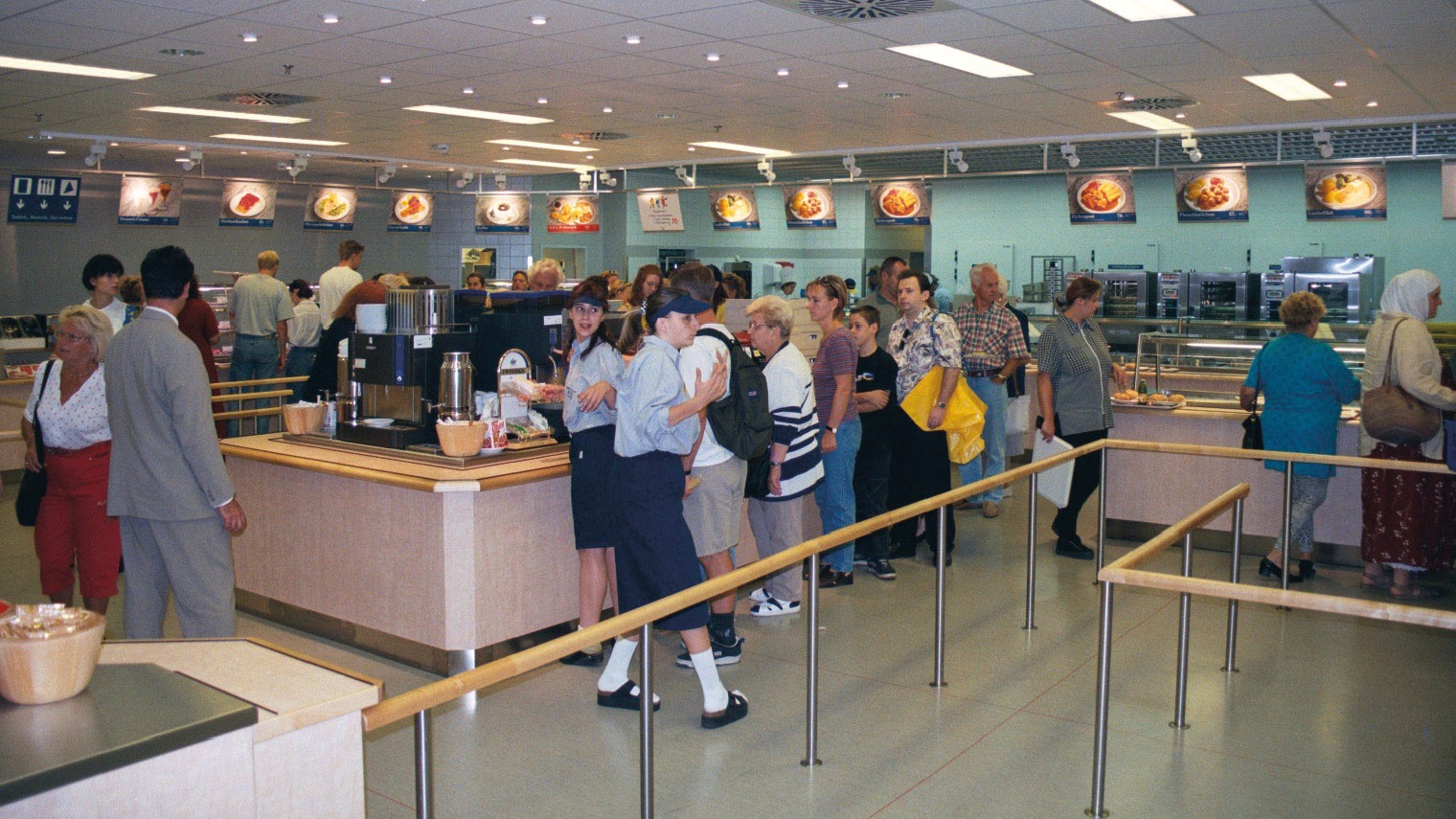 Människor klädda i 1990-talsstil köar i kassaområdet i en IKEA restaurang.
