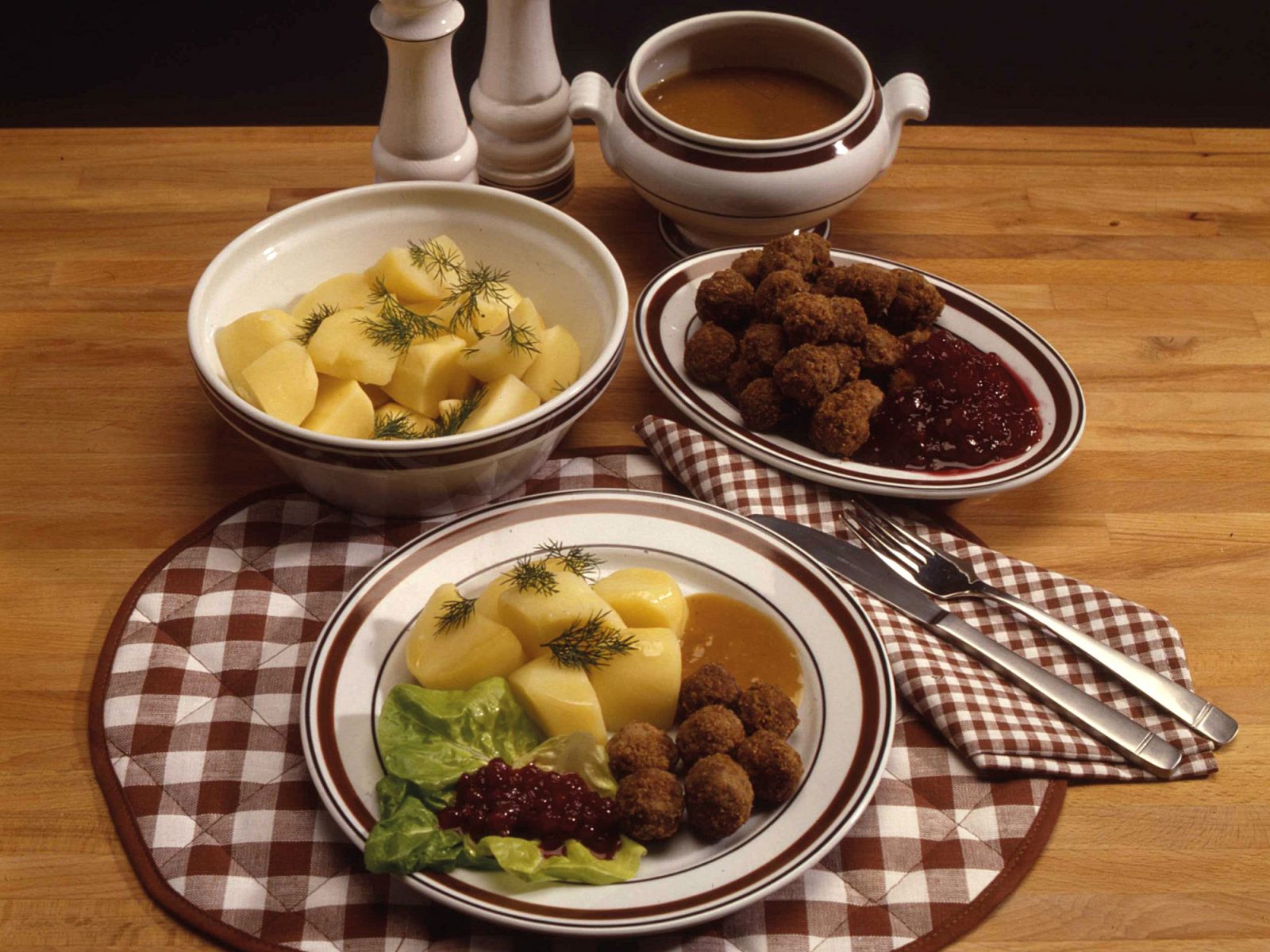 A plate and serving bowls with Swedish meatballs, boiled potatoes, brown sauce and lingonberry jam.