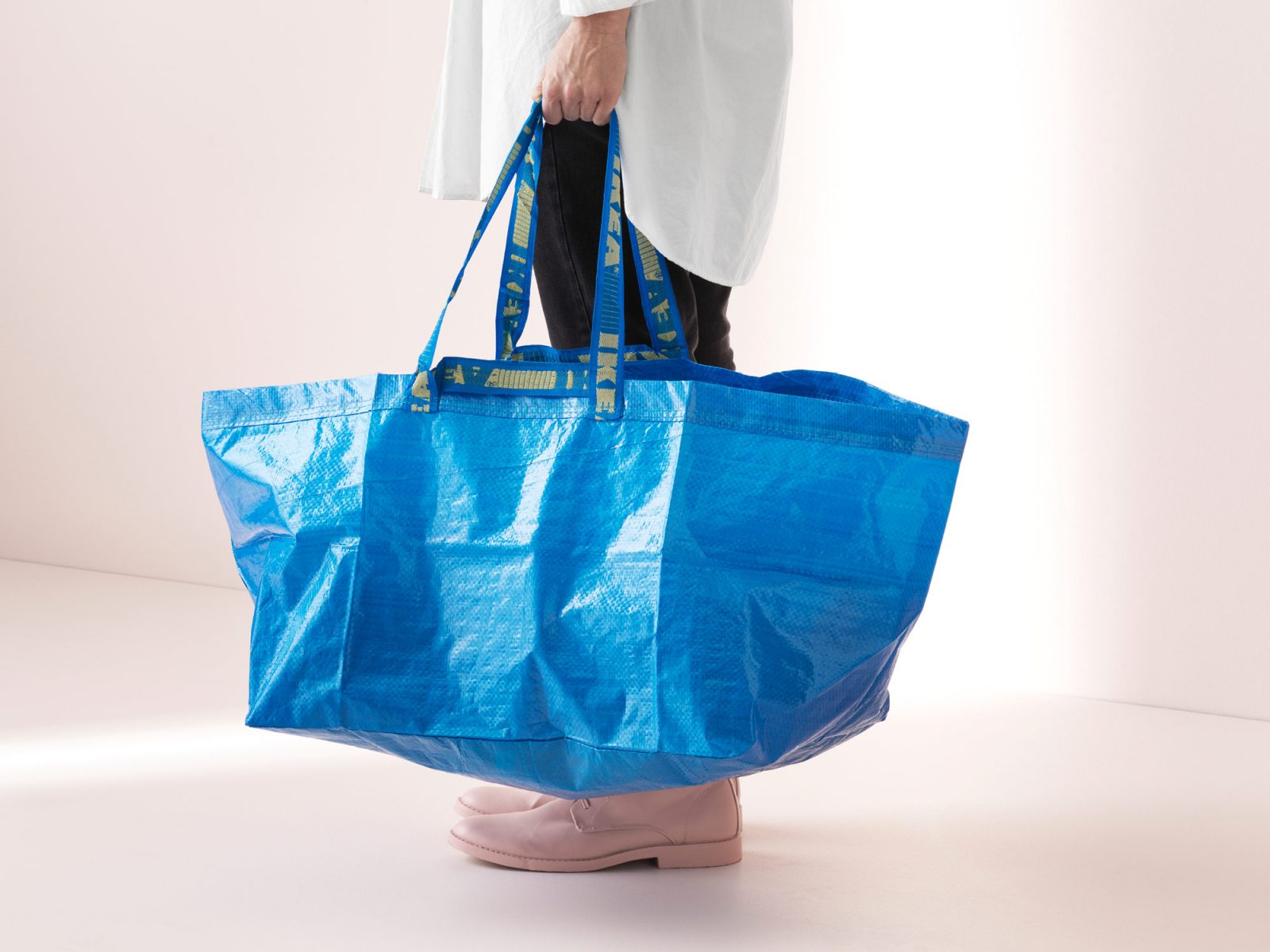 Une personne tient un sac FRAKTA bleu. Seule la partie inférieure du corps est visible.