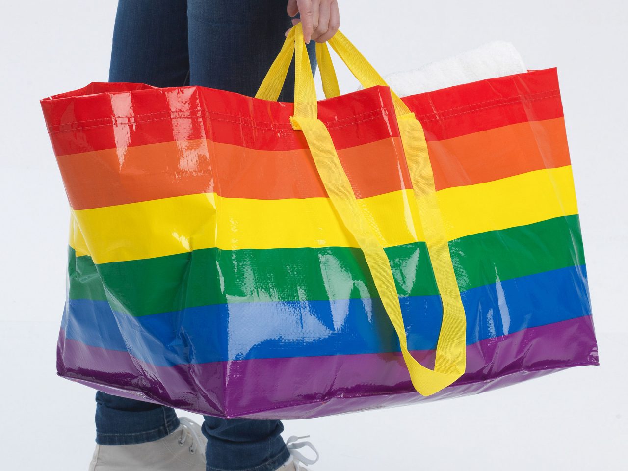 Una persona sostiene una gran bolsa de mano con un estampado arcoíris; solo se ve la parte inferior de su cuerpo.