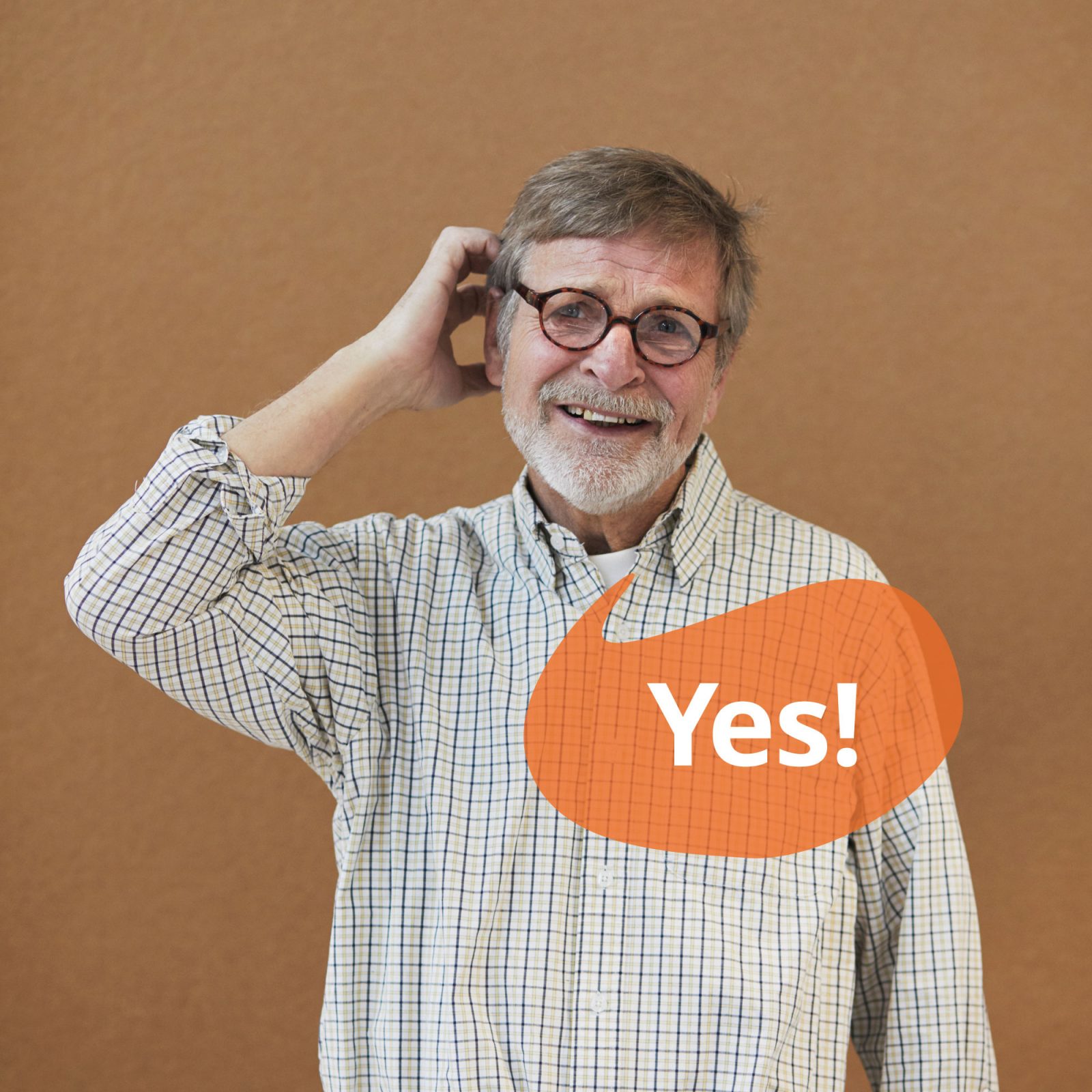 Grey-haired man in glasses and check shirt smiles and scratches his head. A speech bubble contains the text 'Yes'.