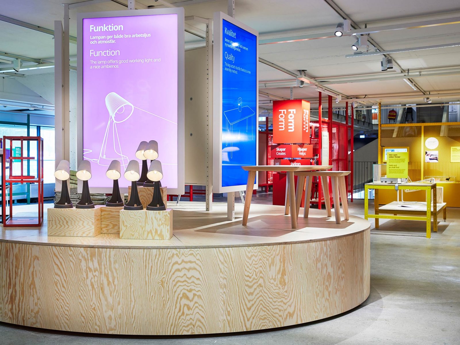 Part of Democratic Design exhibit – light boards in purple and blue with white text behind lamps on wooden boxes and tables.