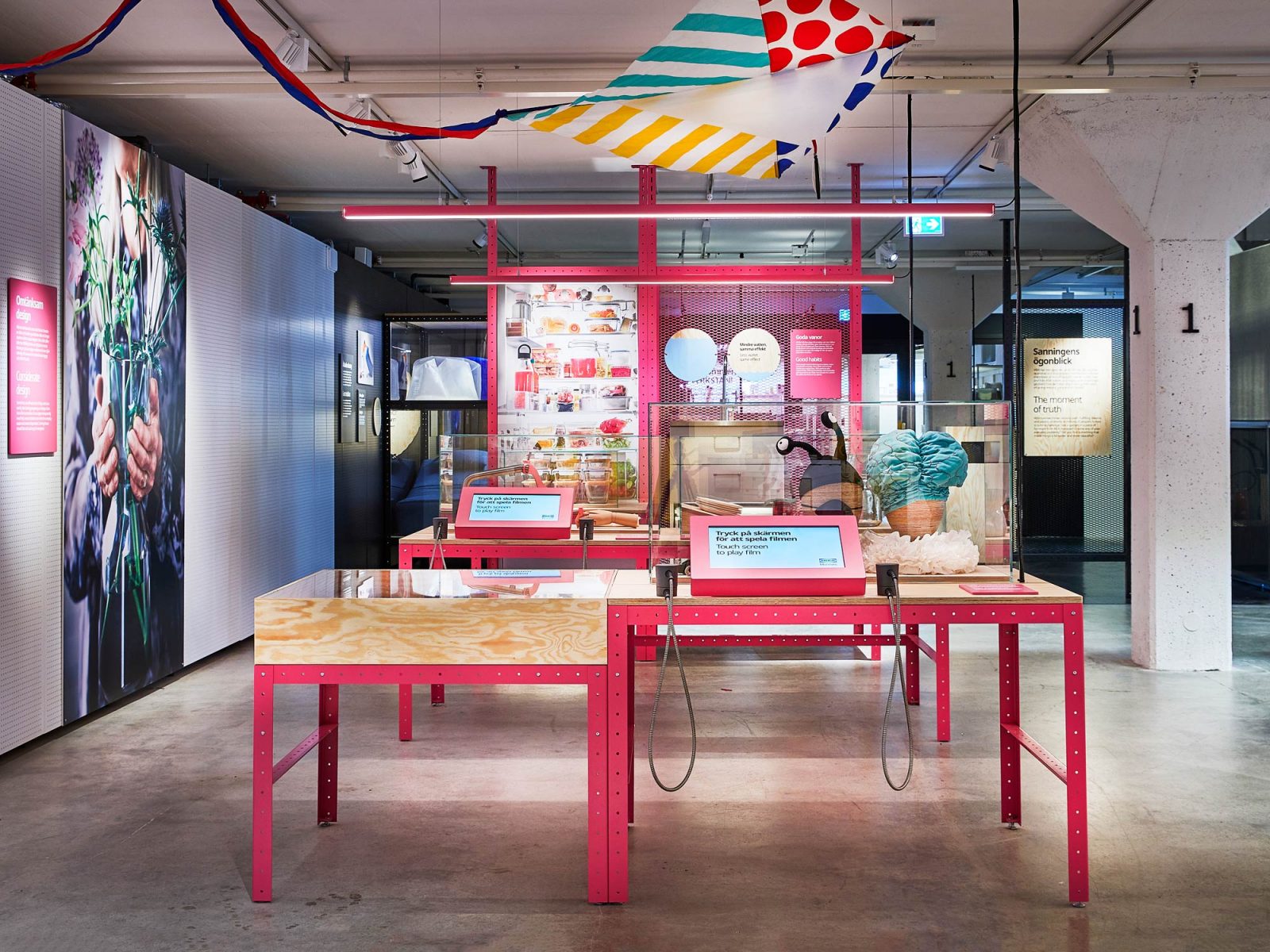 Colourful part of the exhibition Democratic Design with display cases and touch screens on red metal tables.