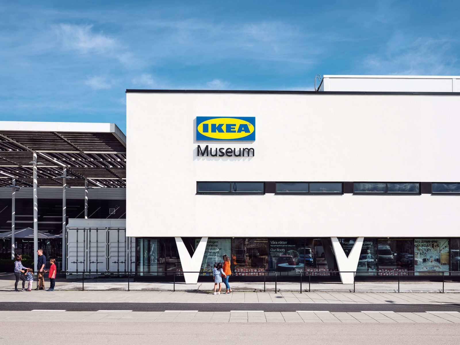 People stand in front of white building with clean lines and v-shaped pillars, sign on facade says IKEA Museum.