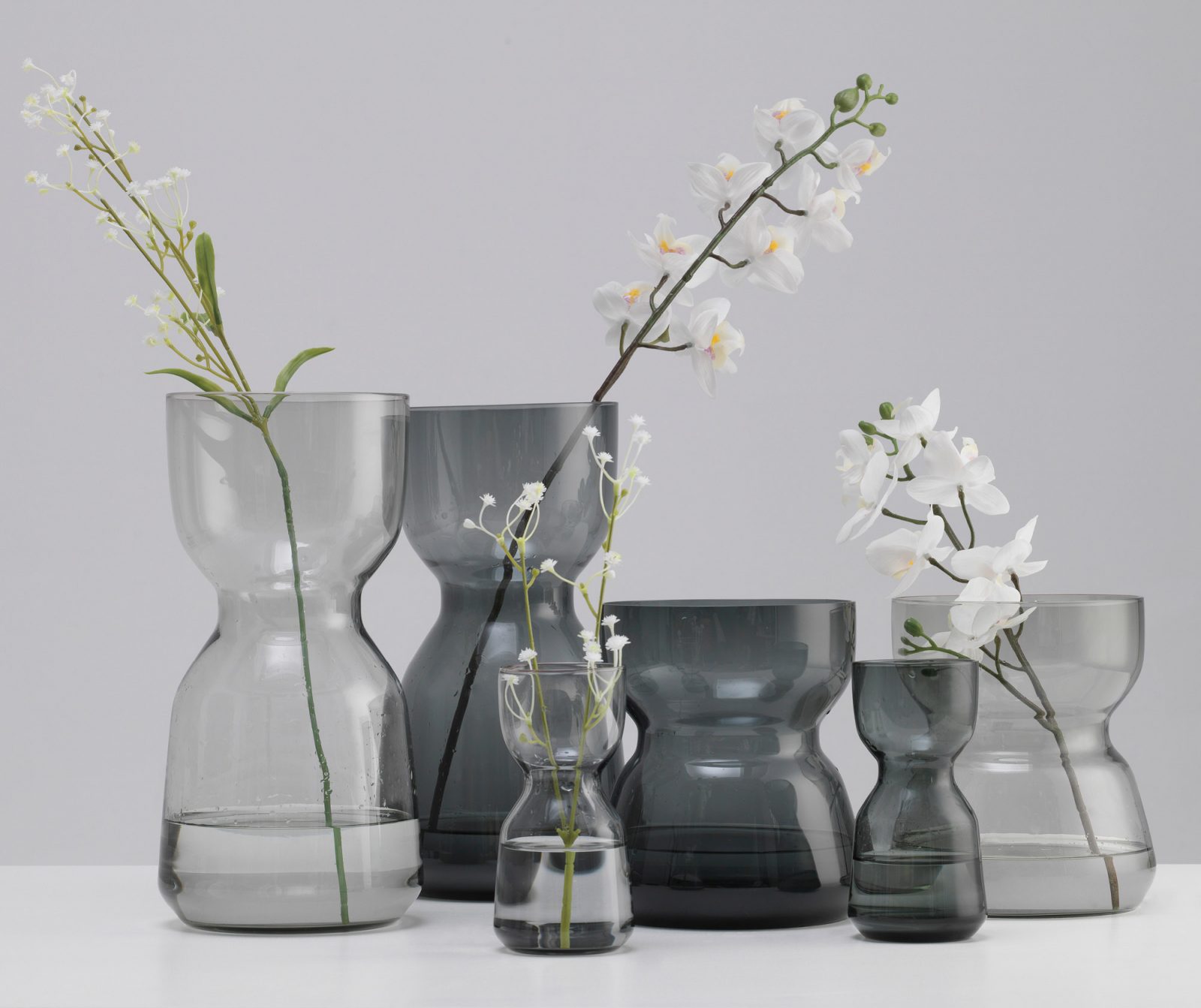 Group of different sized clear and grey glass vases, designed to be easy to lift, carry and wash.