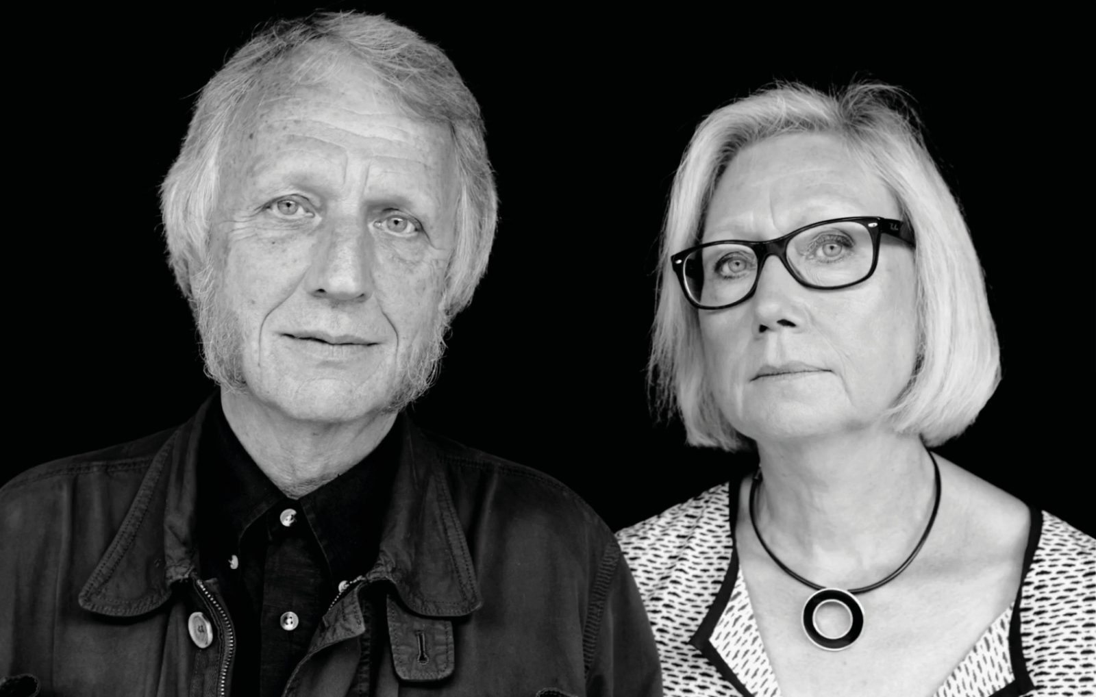 Portrait of grey-blond man and woman, Knut Hagberg and Marianne Hagberg, photographed against a black wall.
