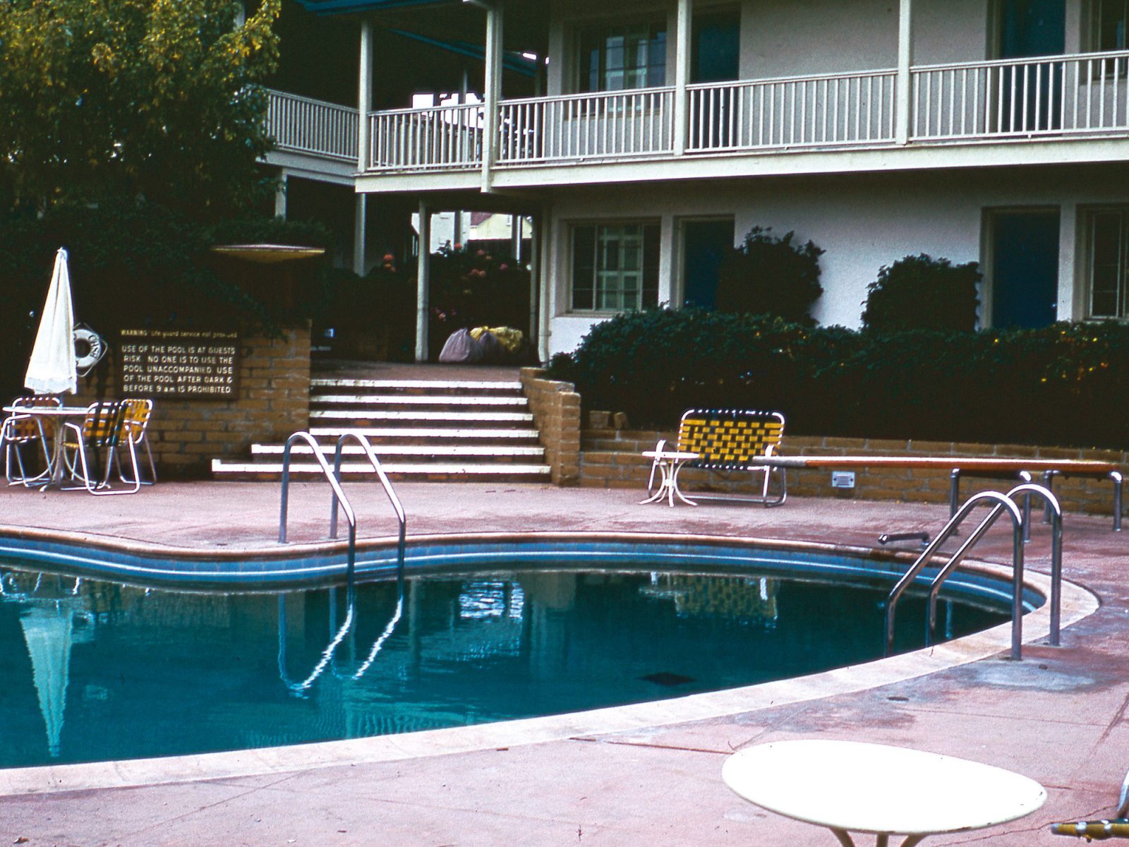 Poolområde med njurformad blå bassäng och solstolar i 1950-talsstil.
