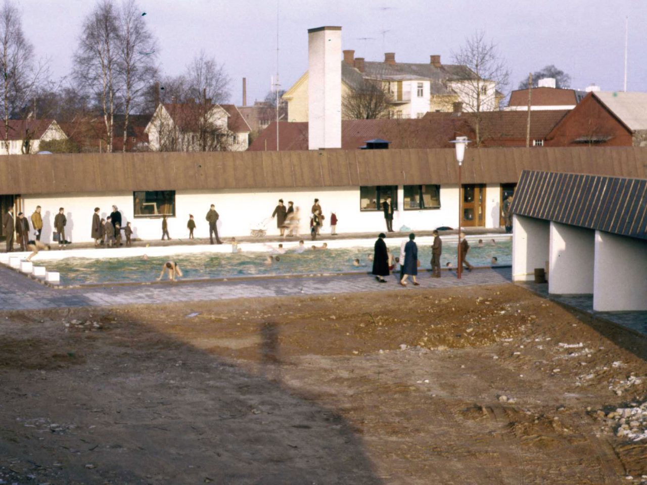 Warmly dressed visitors walk around a motel building and pool in autumn-like weather.