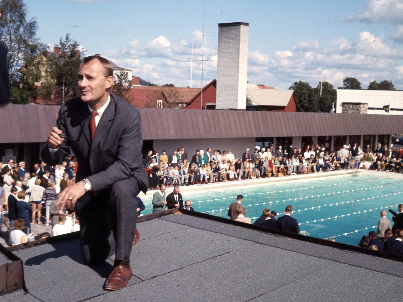 Ingvar Kamprad on a roof, dressed in suit with microphone, a swimming pool and mingling people in the background.