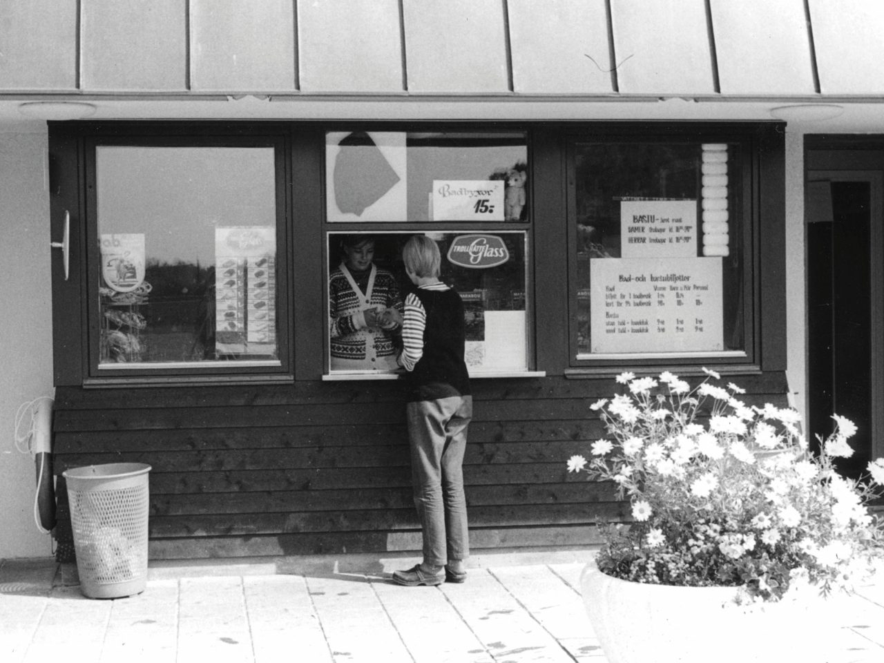 Ung kvinna med kort hår och 1960-tals-kläder handlar i liten kiosk.