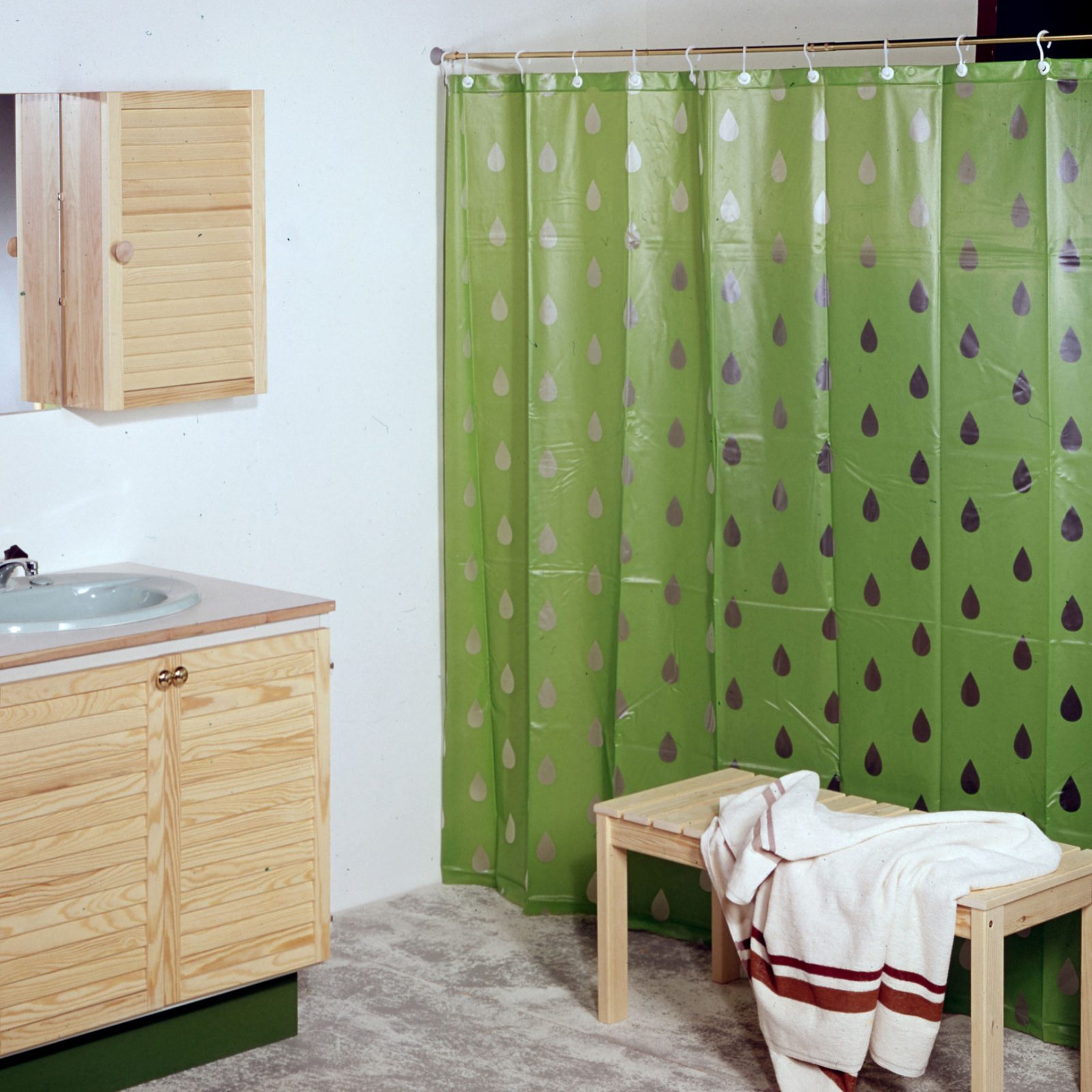 Badrum med träinredning i 1970-talsstil och droppmönstrat grönt duschdraperi i plast, PLASK.