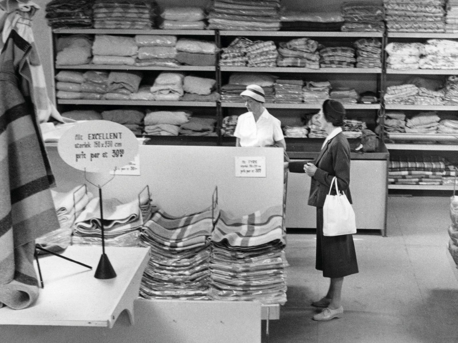 Textile department at IKEA store, two women in 1960s clothes looking at fabrics.