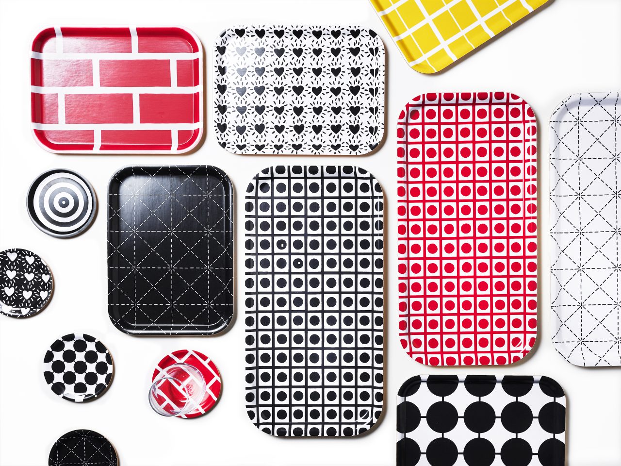 Trays and coasters in different sizes and graphic patterns in red/white, black/white, grey/white and yellow/white.