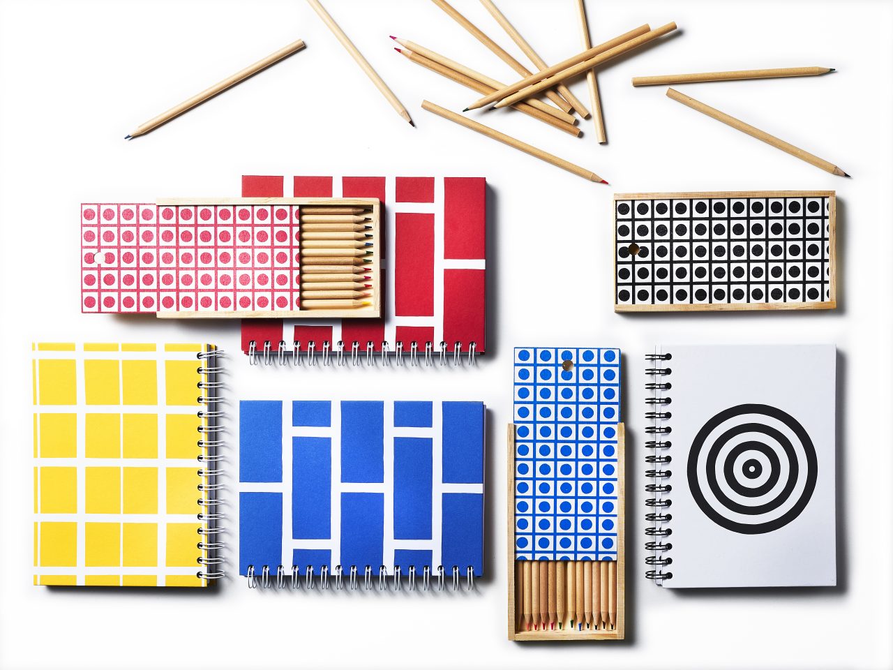 Notebooks, pens and wooden penholders with graphic patterns in blue/white, yellow/white, red/white, black/white.
