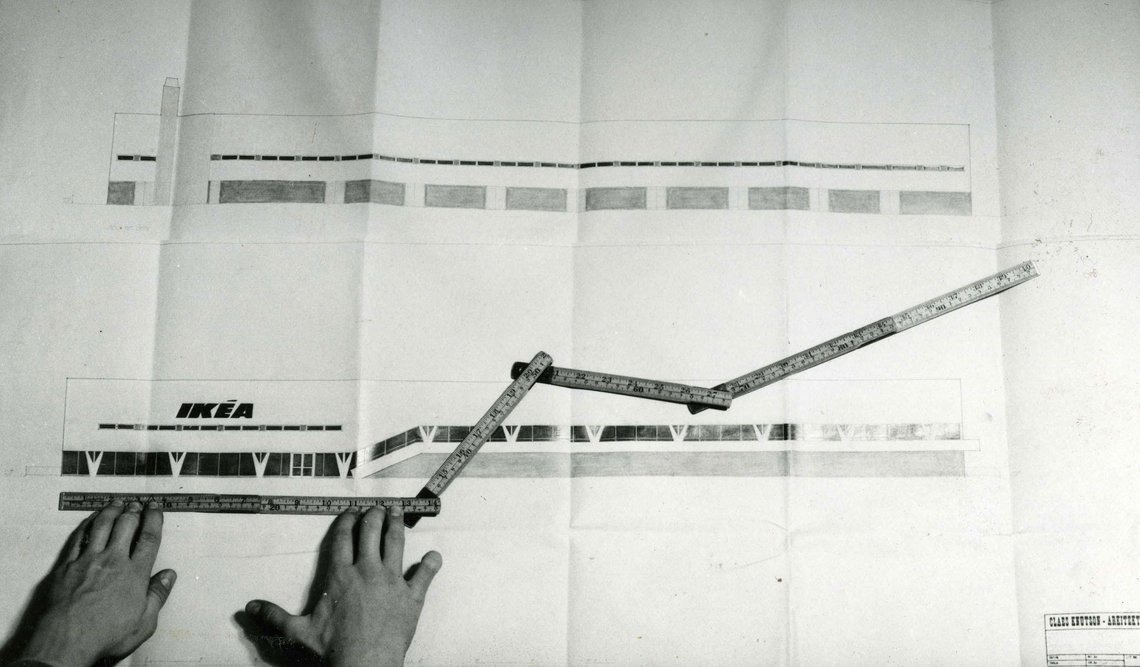Two hands measuring the original architectural designs of the world’s first IKEA store with a folding rule.