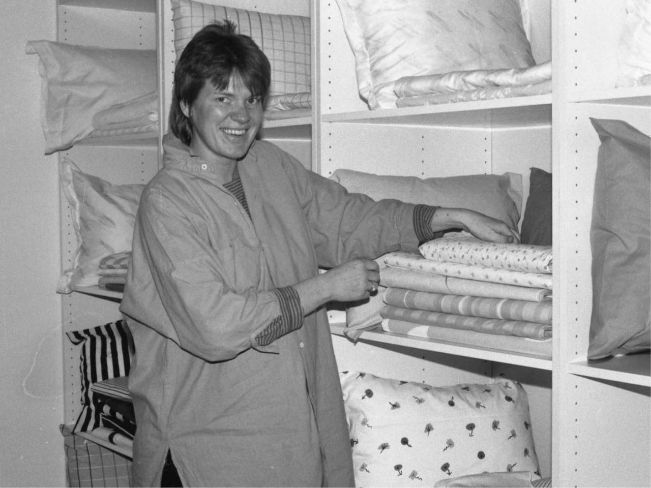Irene Odd, with short hair, stands before shelves of fabric rolls.