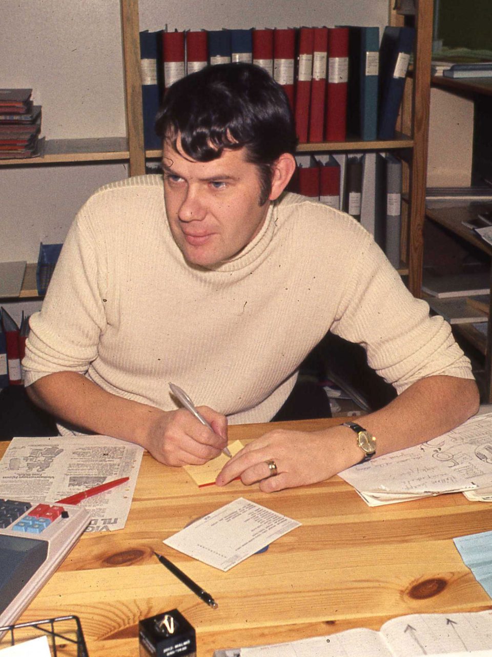 Mörkhårig ung man i vit polotröja arbetar vid skrivbord, Lars Göran Peterson, LGP.