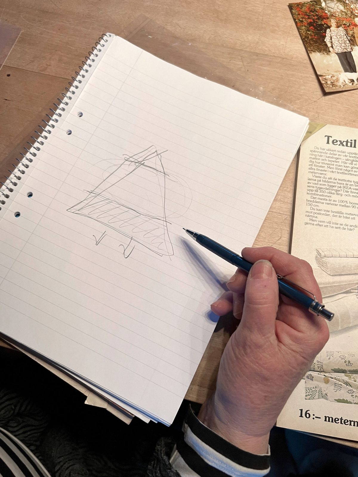 Close-up of a woman's hand sketching a triangular diagram in a notebook.