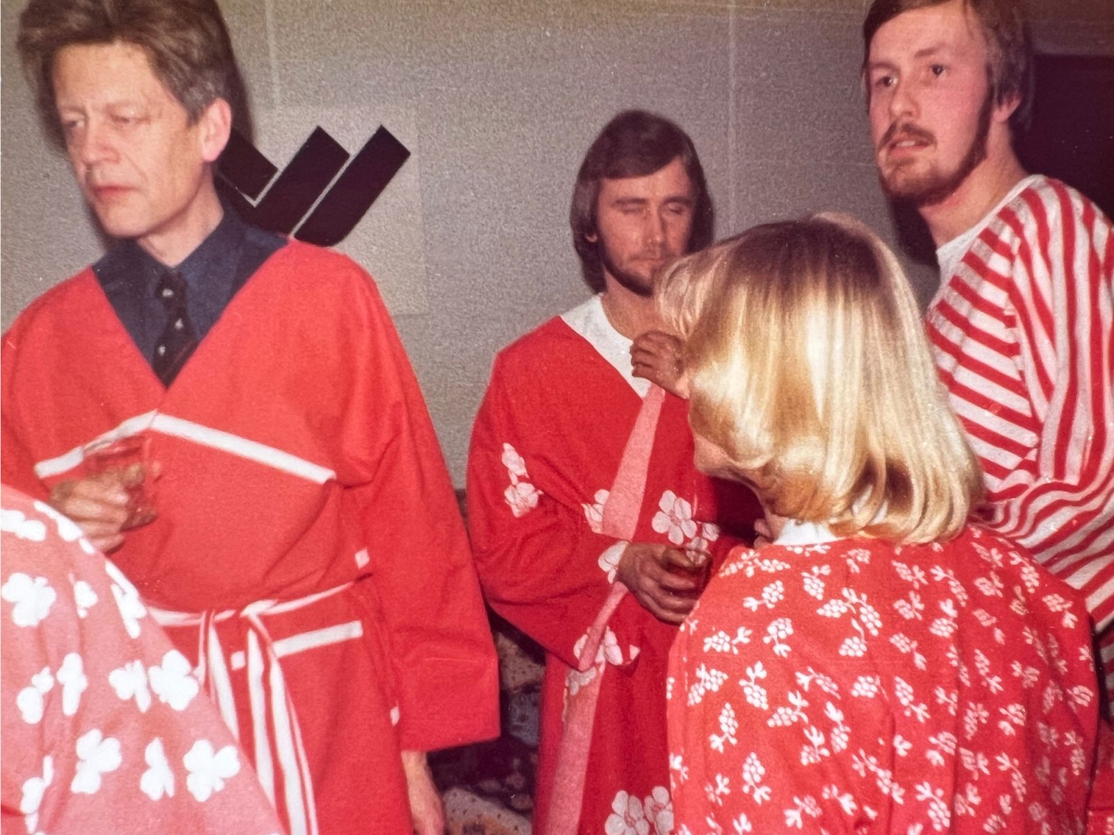 Group of men and a woman in red patterned fabric coats, holding drinks glasses.