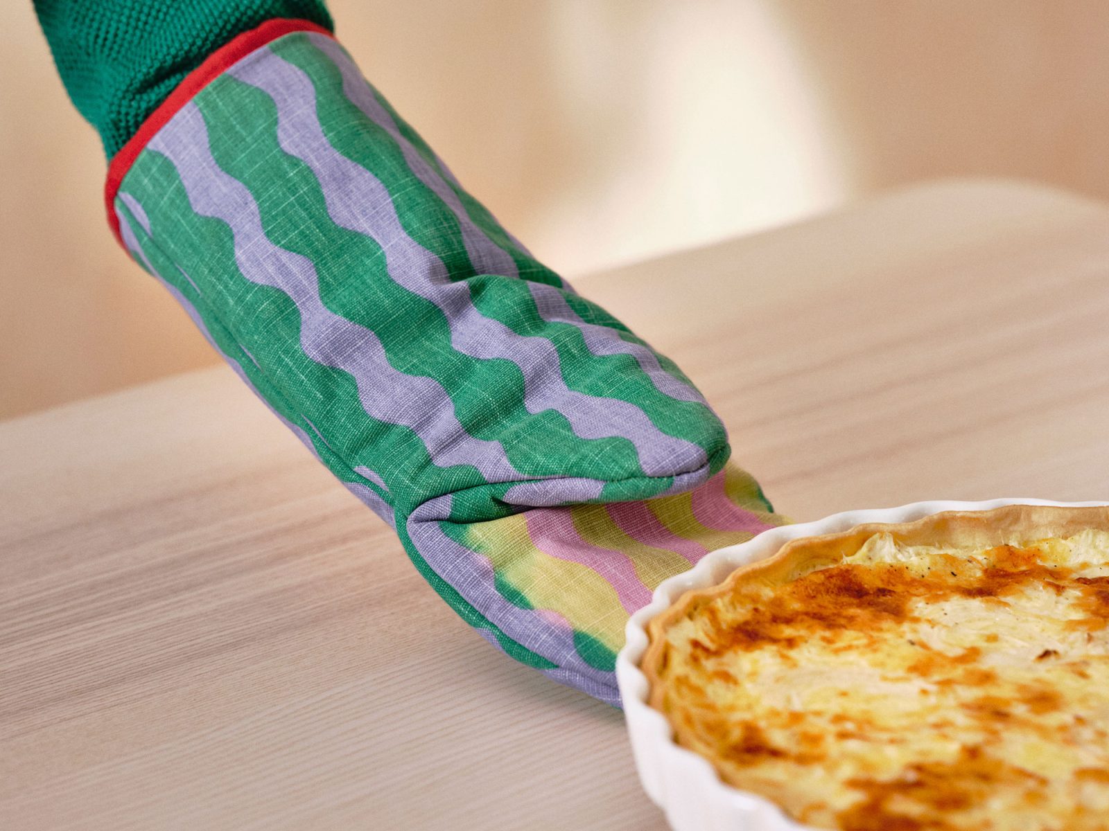 Person wearing green-blue-red oven glove moves to lift a hot pie dish.