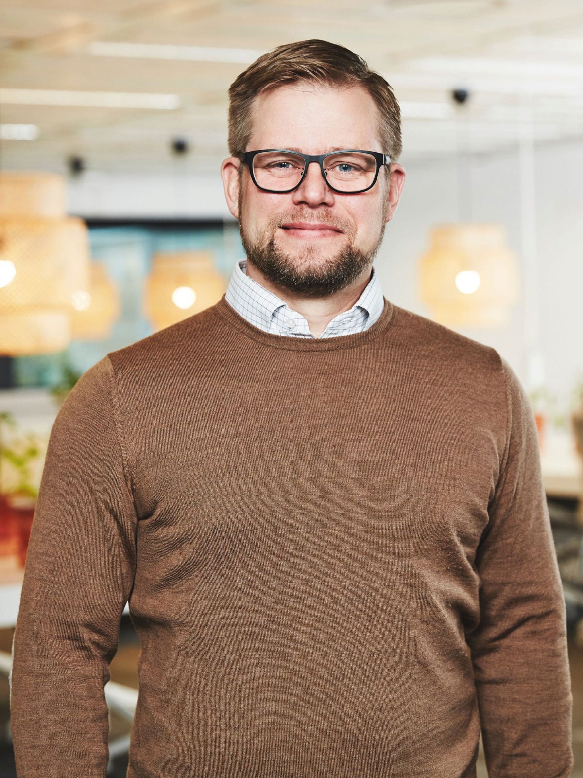 Man med kort brunt hår, glasögon och brun tröja över rutig skjorta, Nils Månsson.