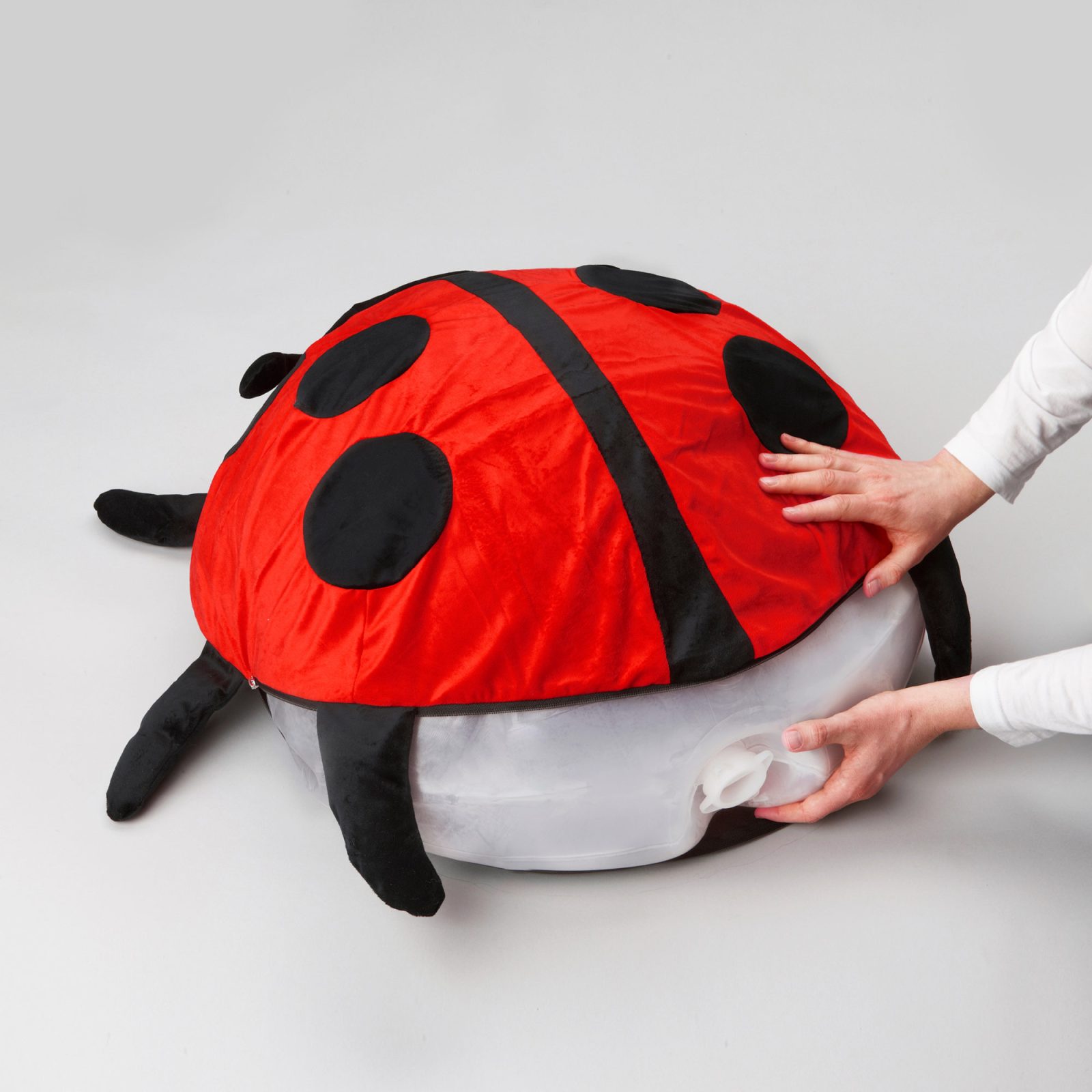 Close-up of hands fitting a cover designed as a ladybird on inflated plastic pillow.