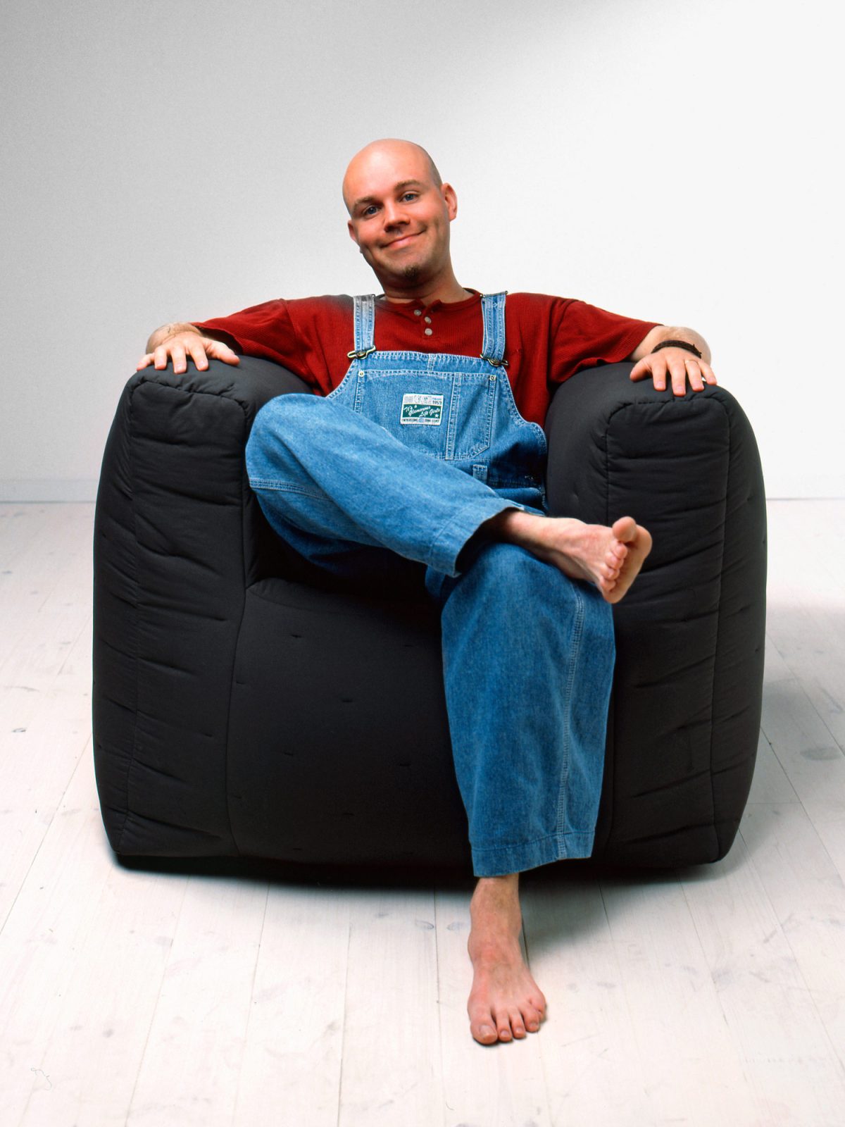 Smiling young man in dungarees sits in chubby dark blue armchair from the a.i.r series.