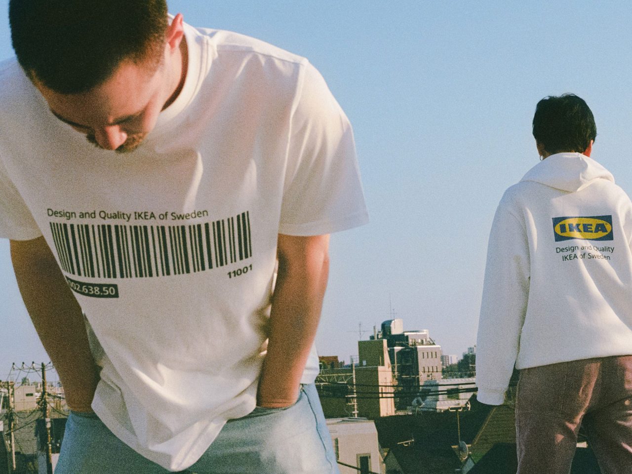 Two people on a rooftop, one in a white T-shirt with a large black barcode, the other in a white hoodie with IKEA text.