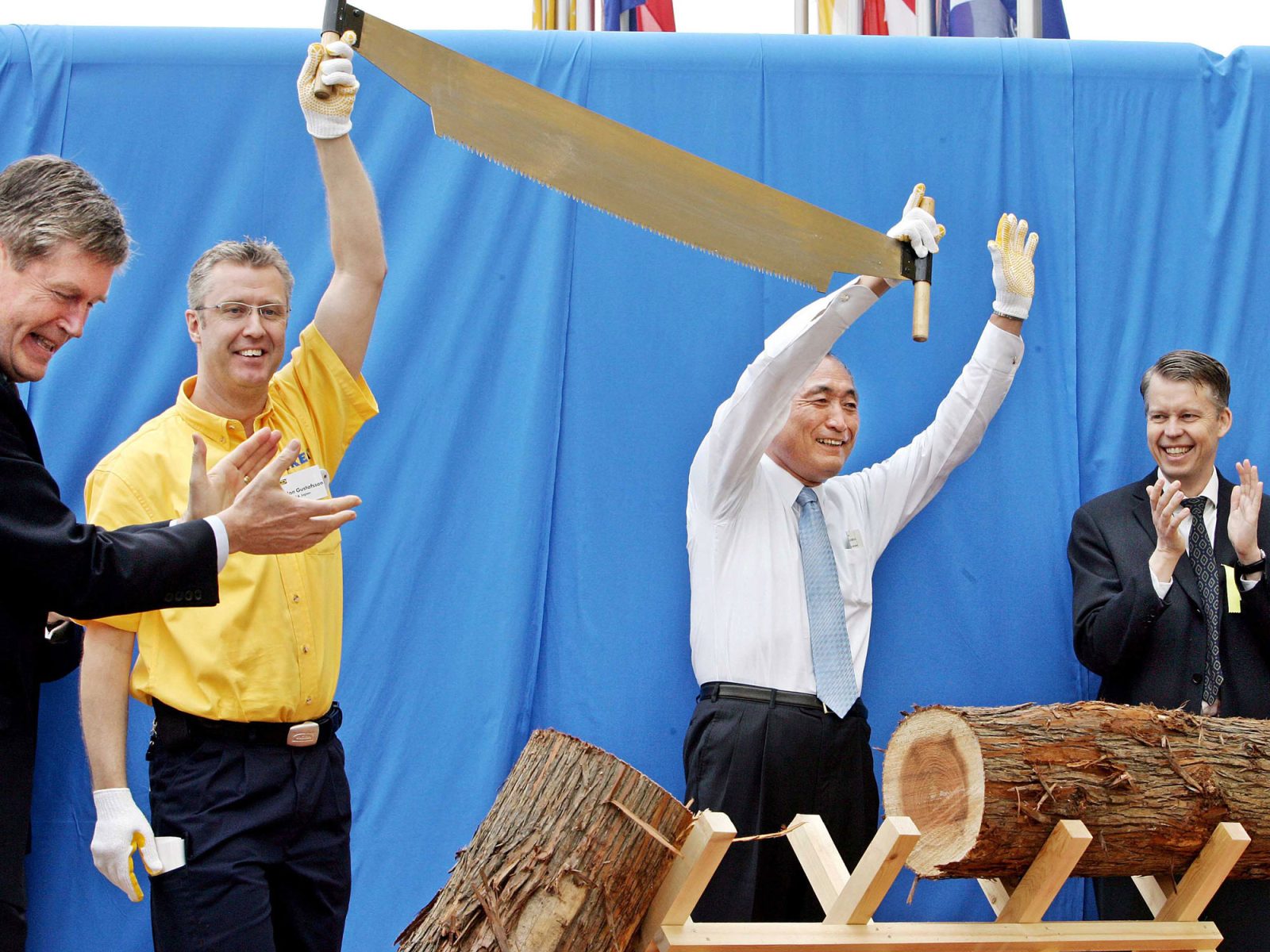Two happy men proudly lifting a large saw, in front of them lies a large log split in two.