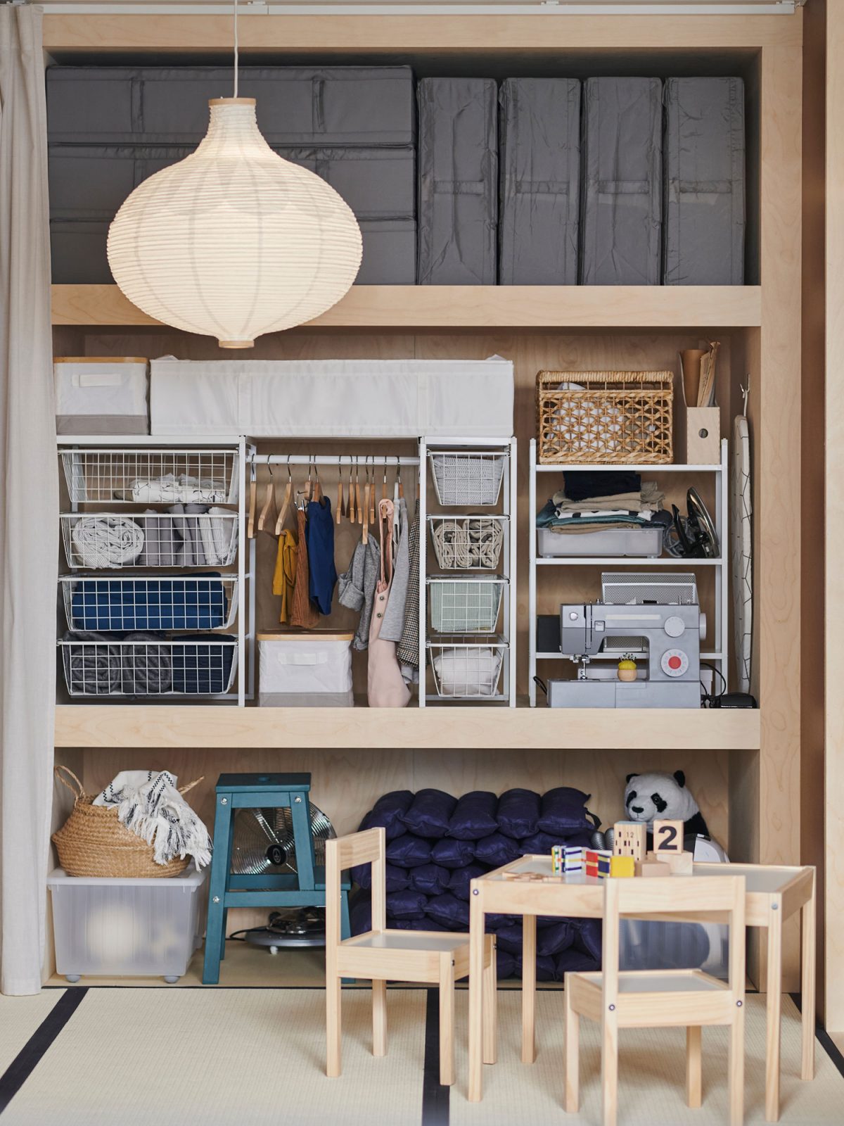 Large deep wardrobe, neatly organised with storage boxes and metal baskets, a large rice paper lamp in the foreground.