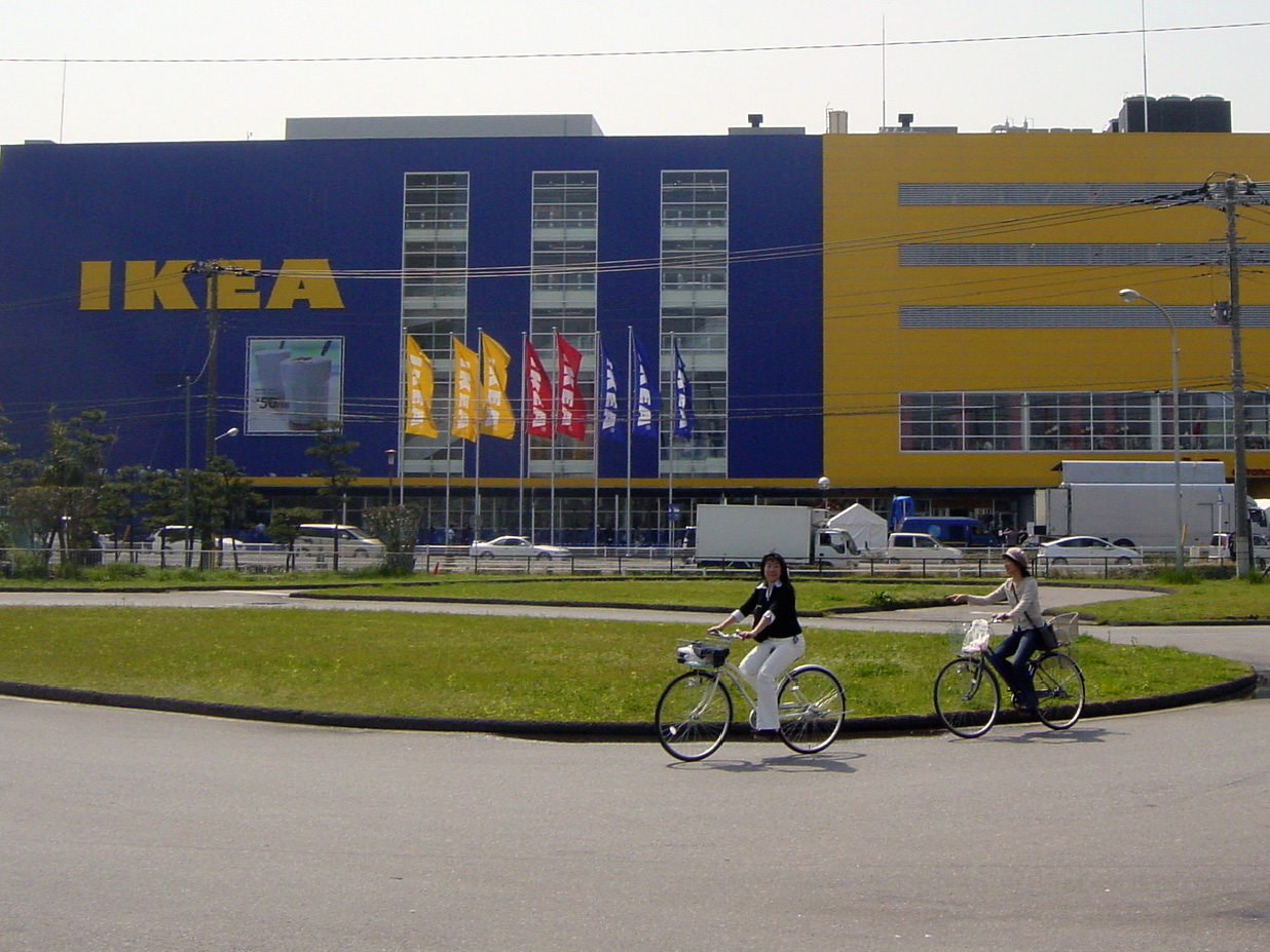 Två kvinnor cyklar framför ett stort blågult IKEA varuhus.